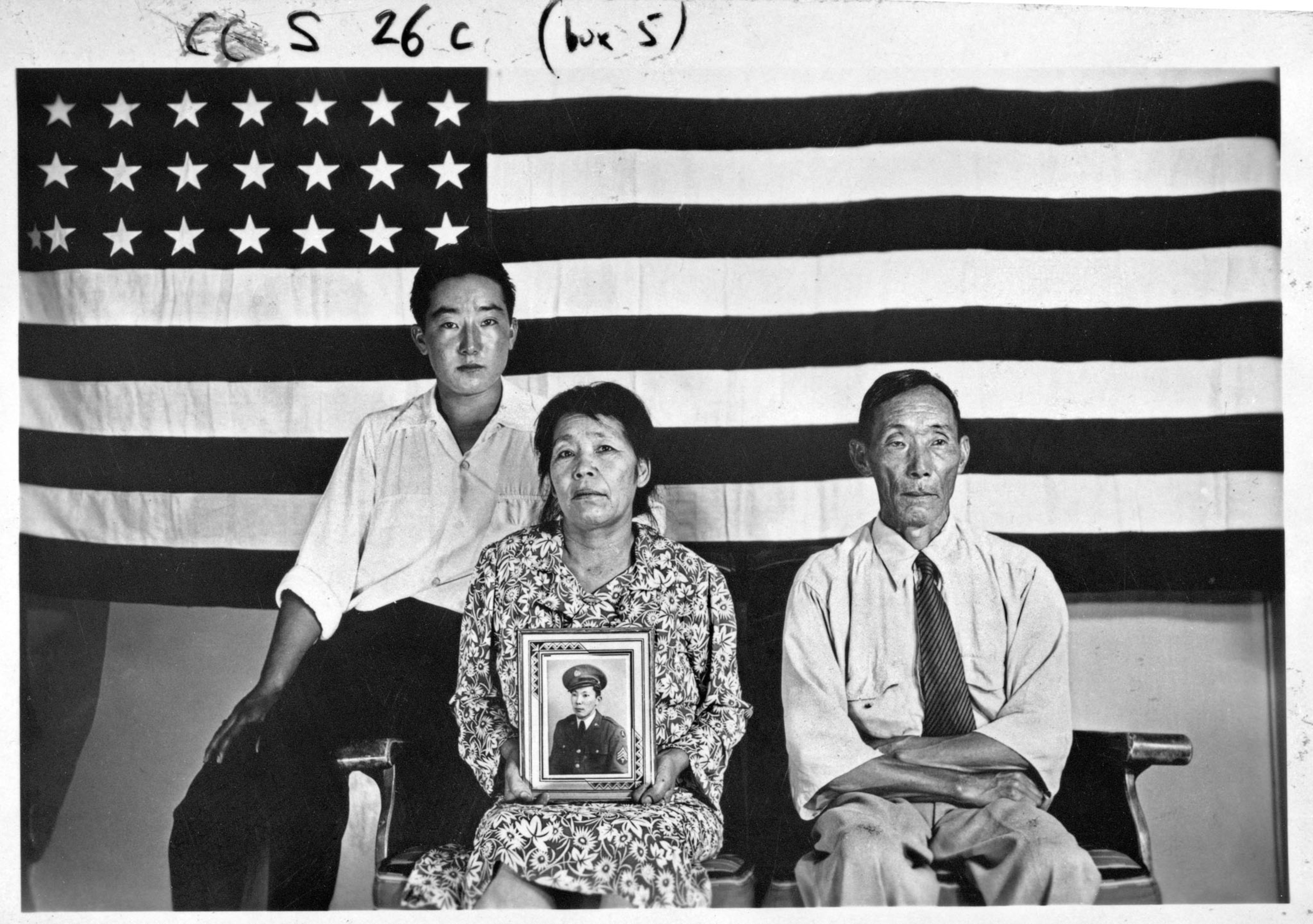 two men and a women sitting in front of a U.S. flag, the woman hold a picture frame