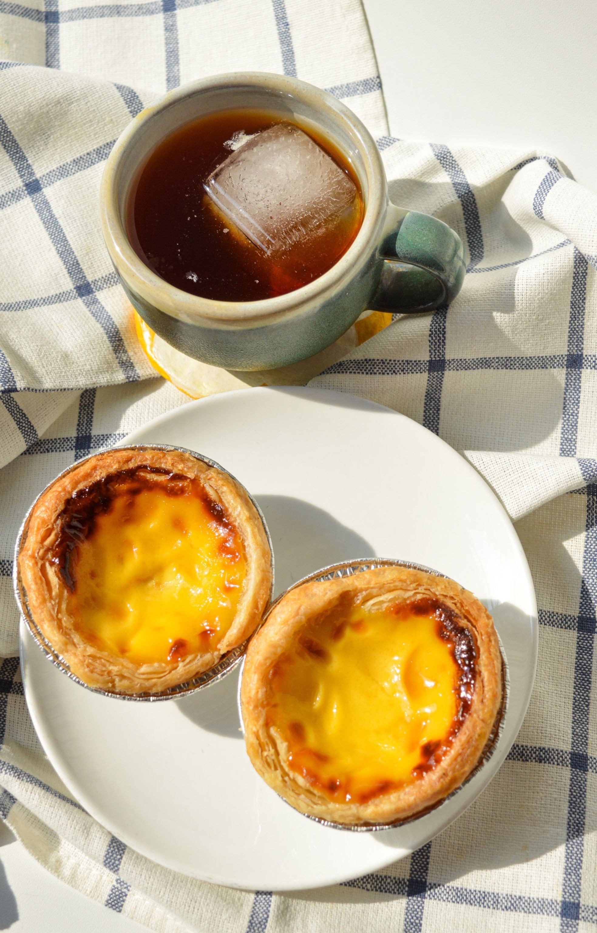 Two small pastries sit on a white plate next to a cup of iced coffee.
