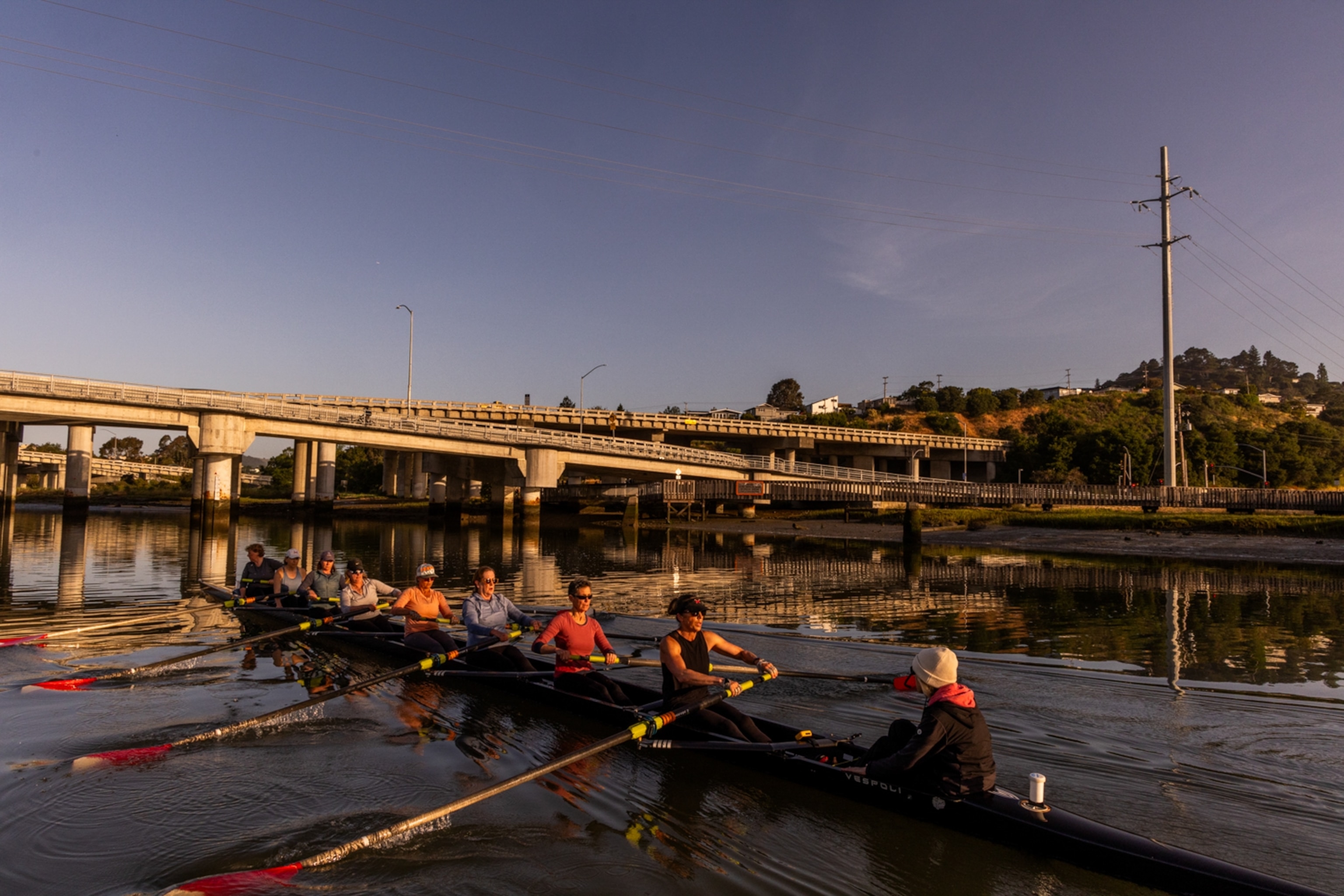 Deep blue skies and bridges in the background as the rowers practice on the water.