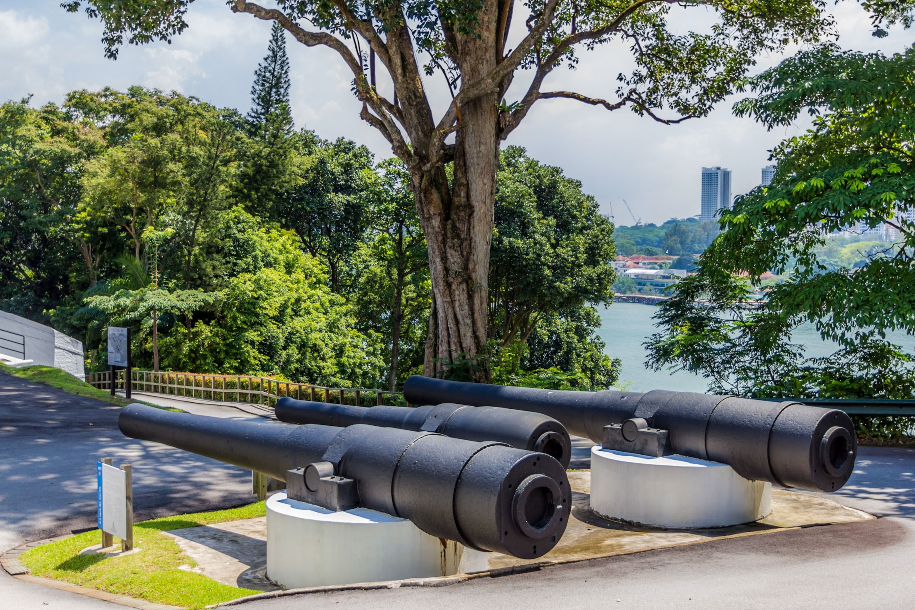 two large canon barrels are seen in the foreground overlooking a body of water and city skyline in Singapore