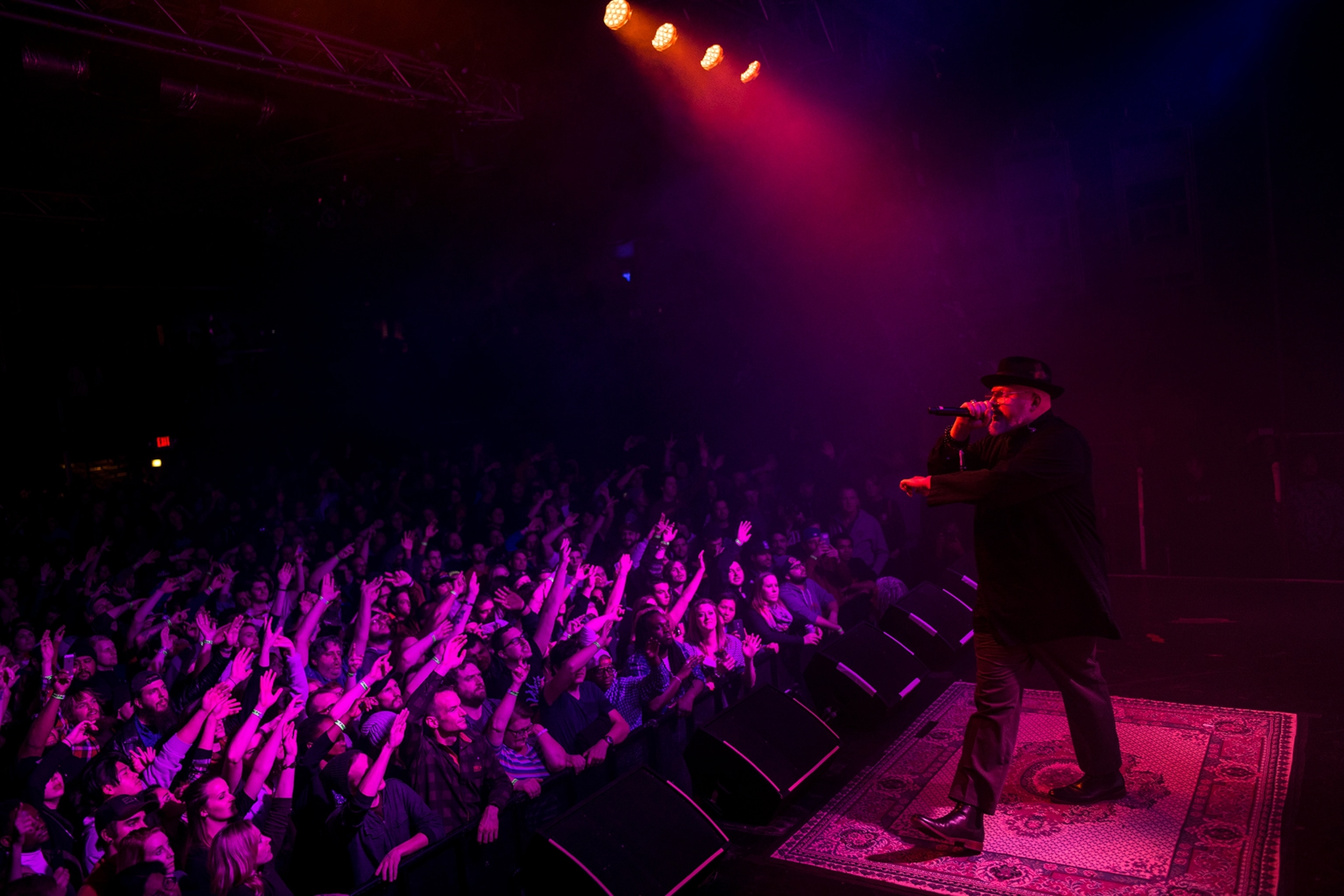 a rapper performing under pink neon lights as the people raise their hands up