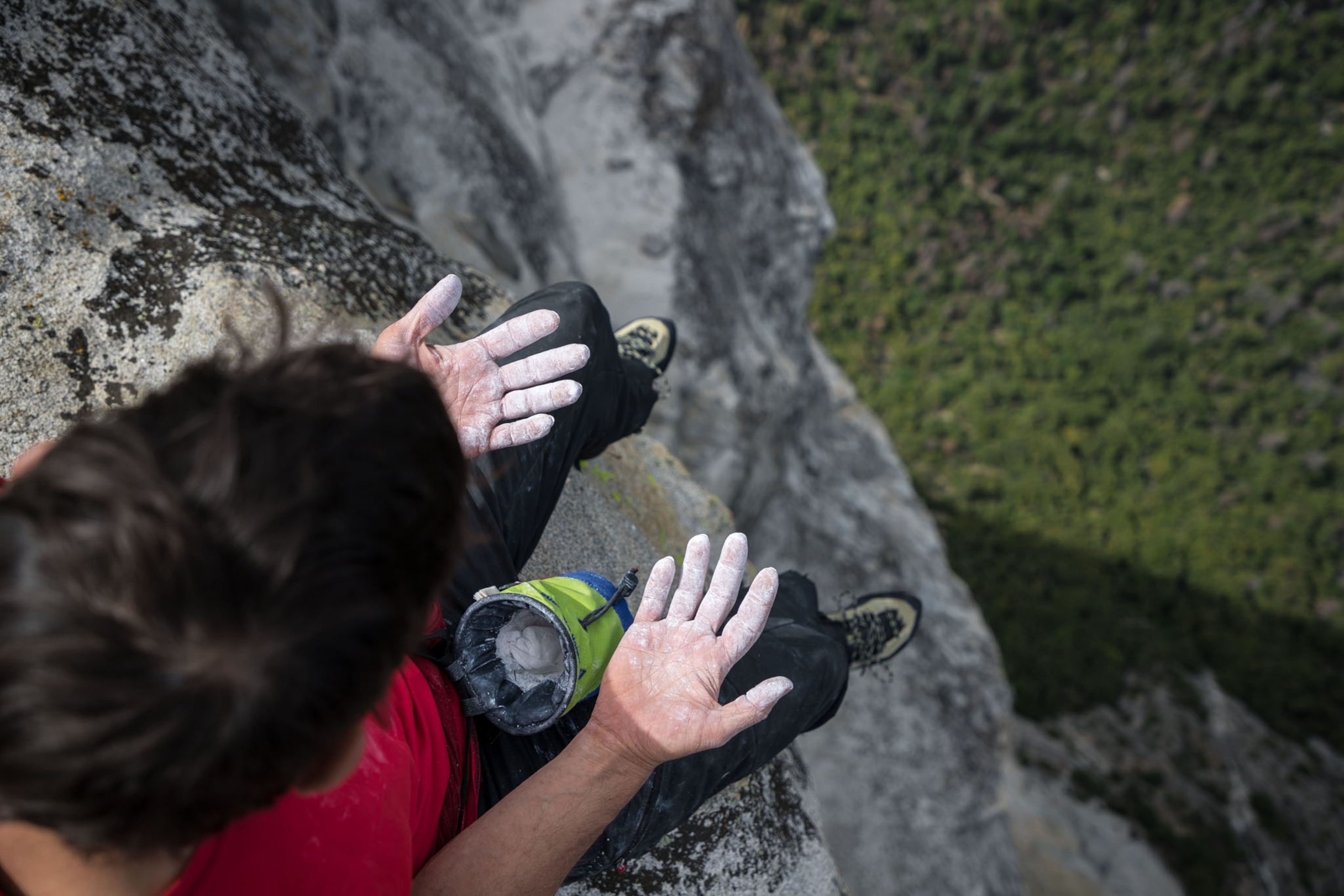 a man looking down at chalk covered hands at the top of a mountain