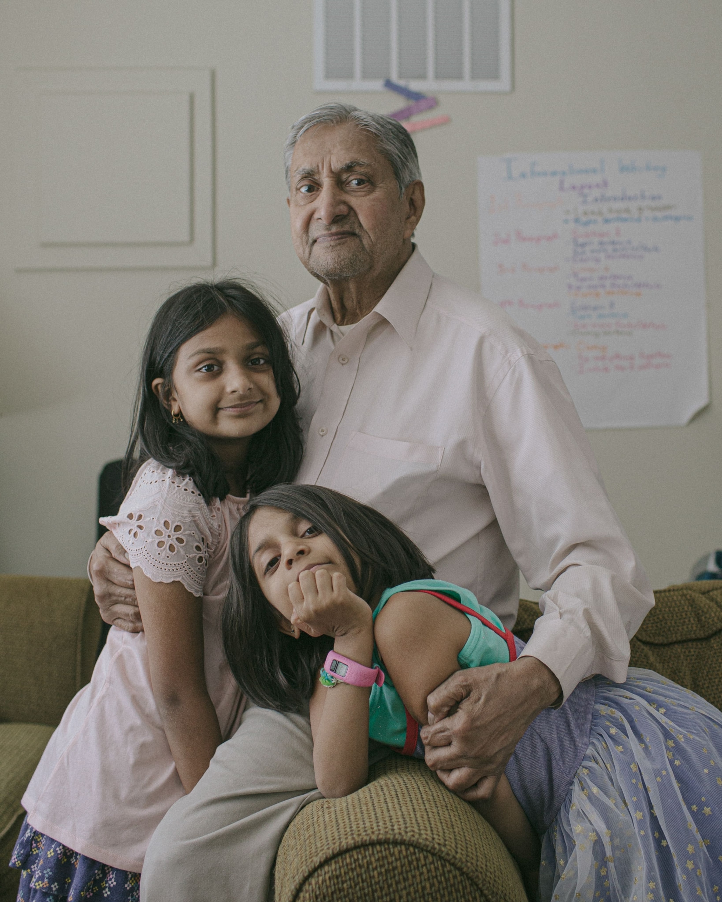 a grandfather poses for a portrait with his two granddaughters