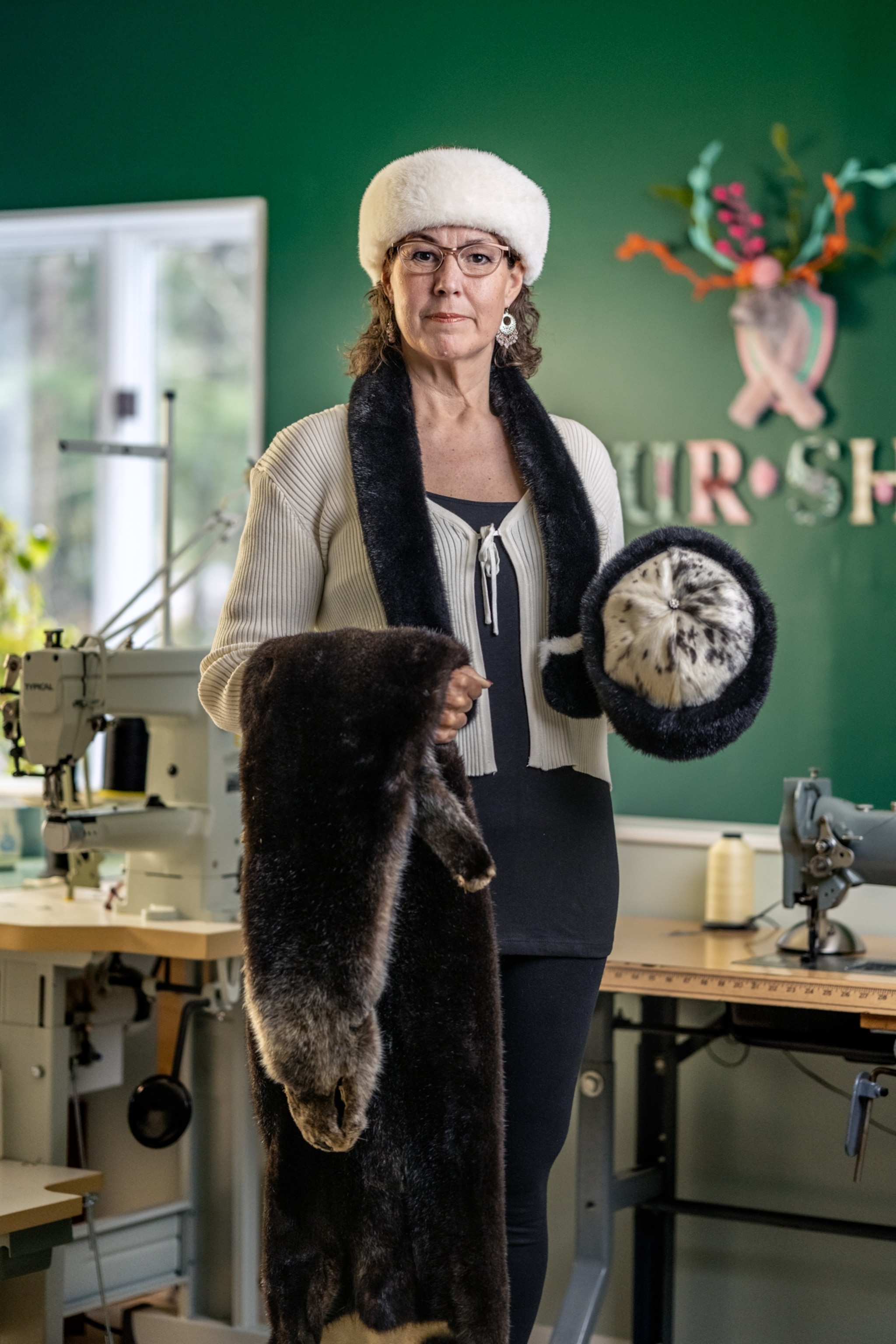 Picture of a woman holding an otter pelt, a hat made from otter fur and wearing a hat made from otter fur.