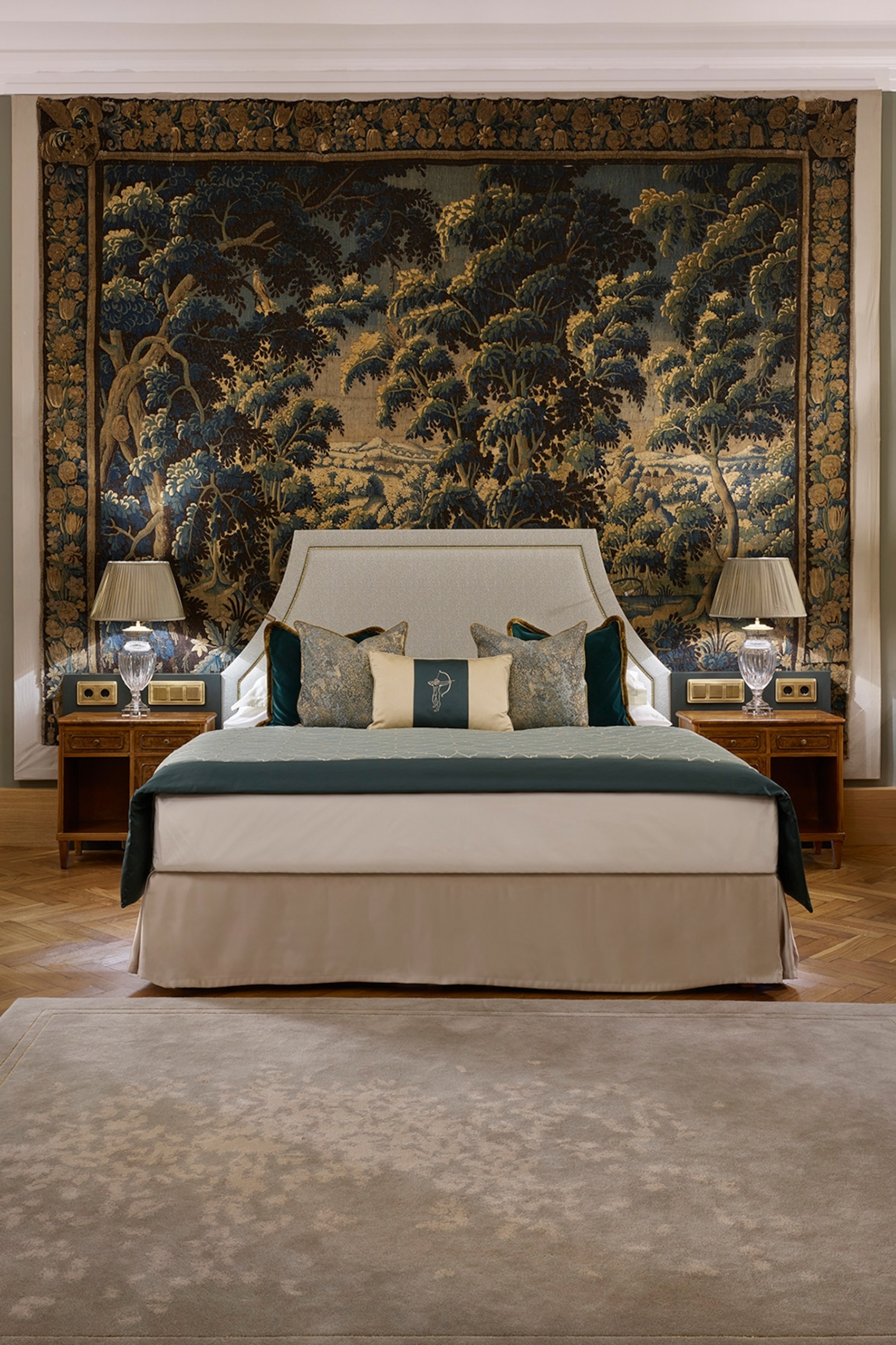 A pompous yet modern hotel room with a sleek Queen bed and a tapestry covering the wall behind.