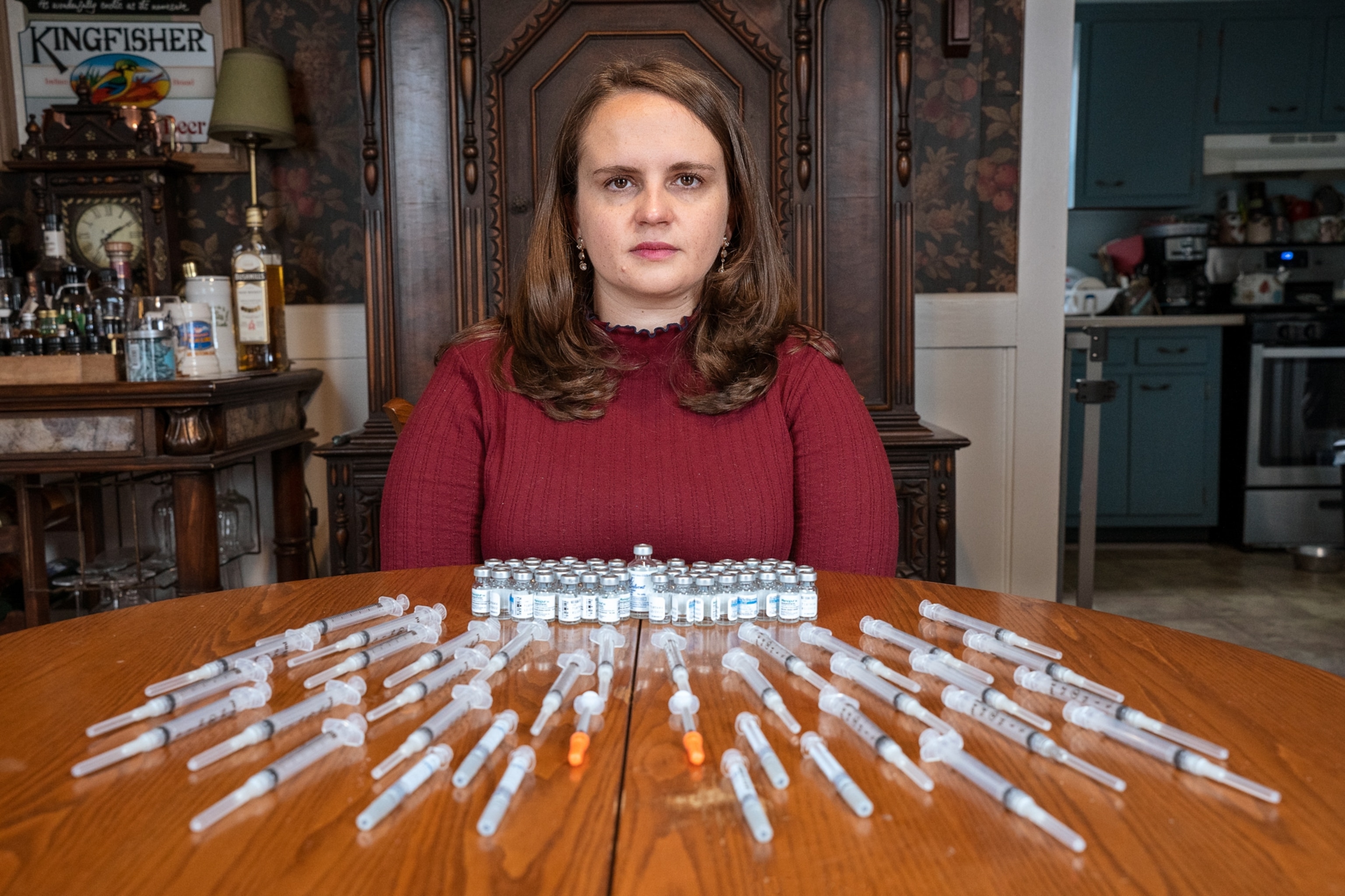 A woman sits for a portrait before a table arranged with syringes and hormone vials she uses for her egg freezing cycles.