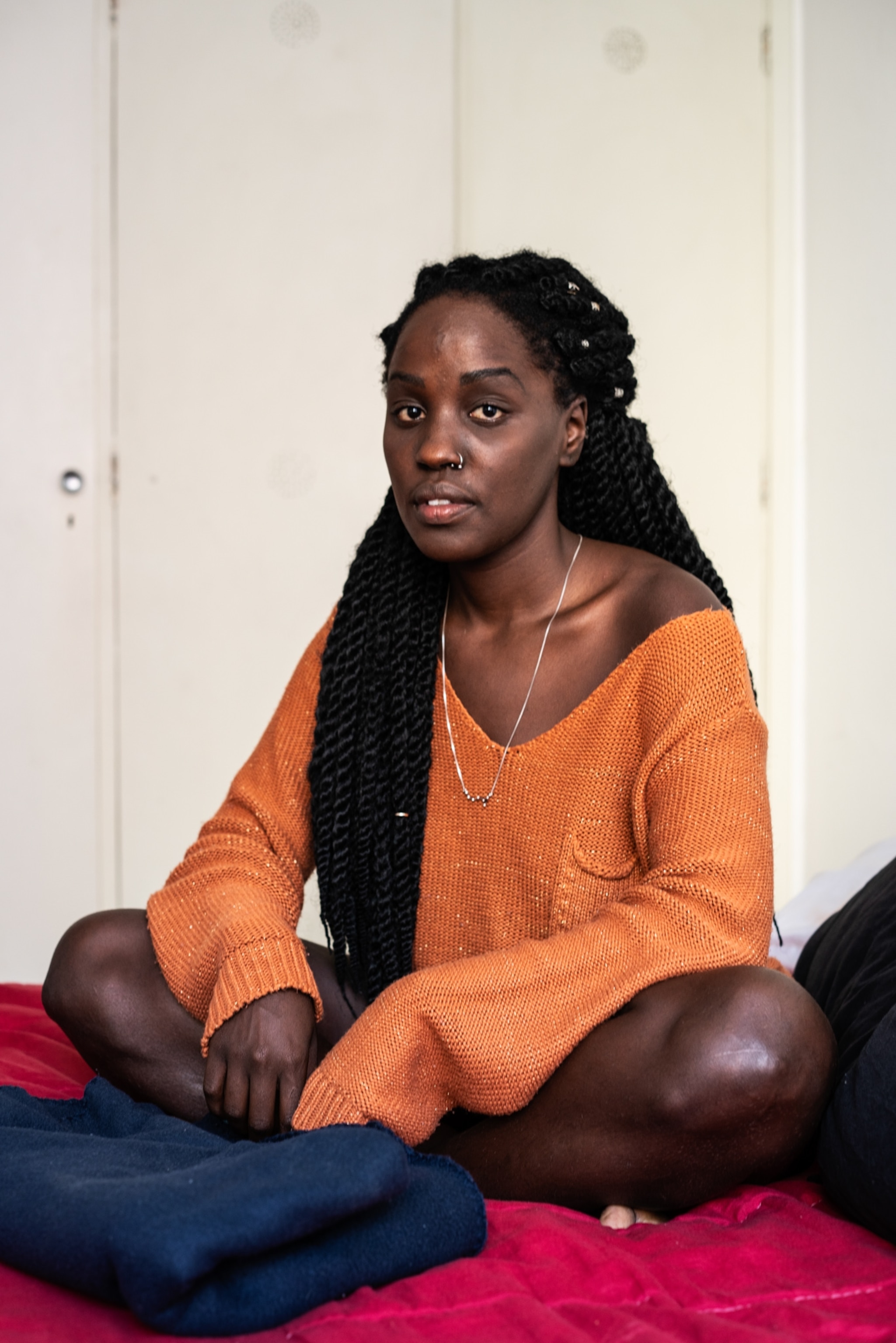 a woman with long braids wearing orange sitting for a portrait