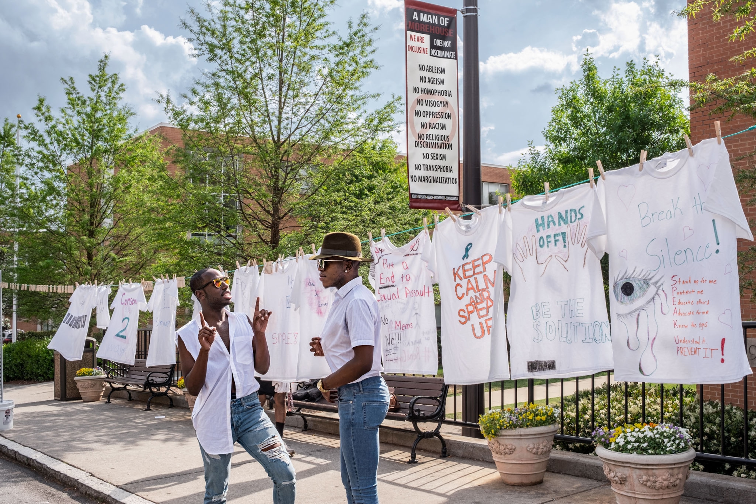 two black students having a discussion in front of a line of hanging white t-shirts
