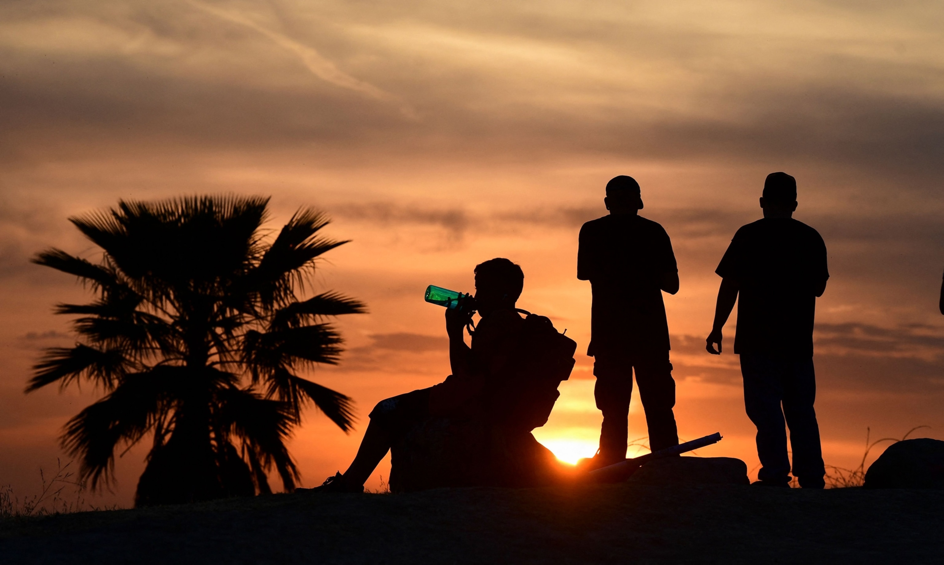 people watching the sun set while a child drinks from a water bottle during a heatwave