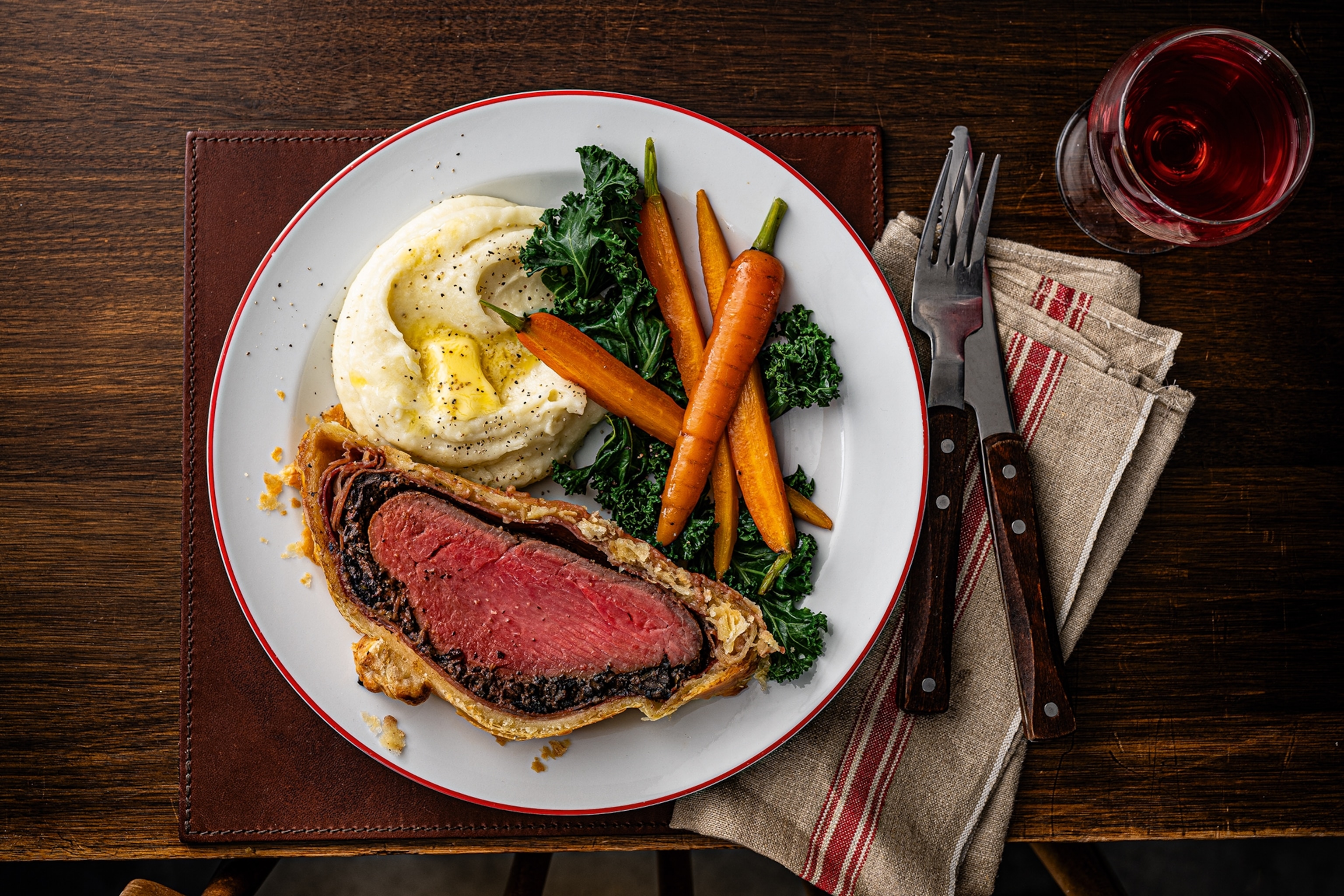 Slice of beef wellington served alongside mash potato and vegetables on a plate