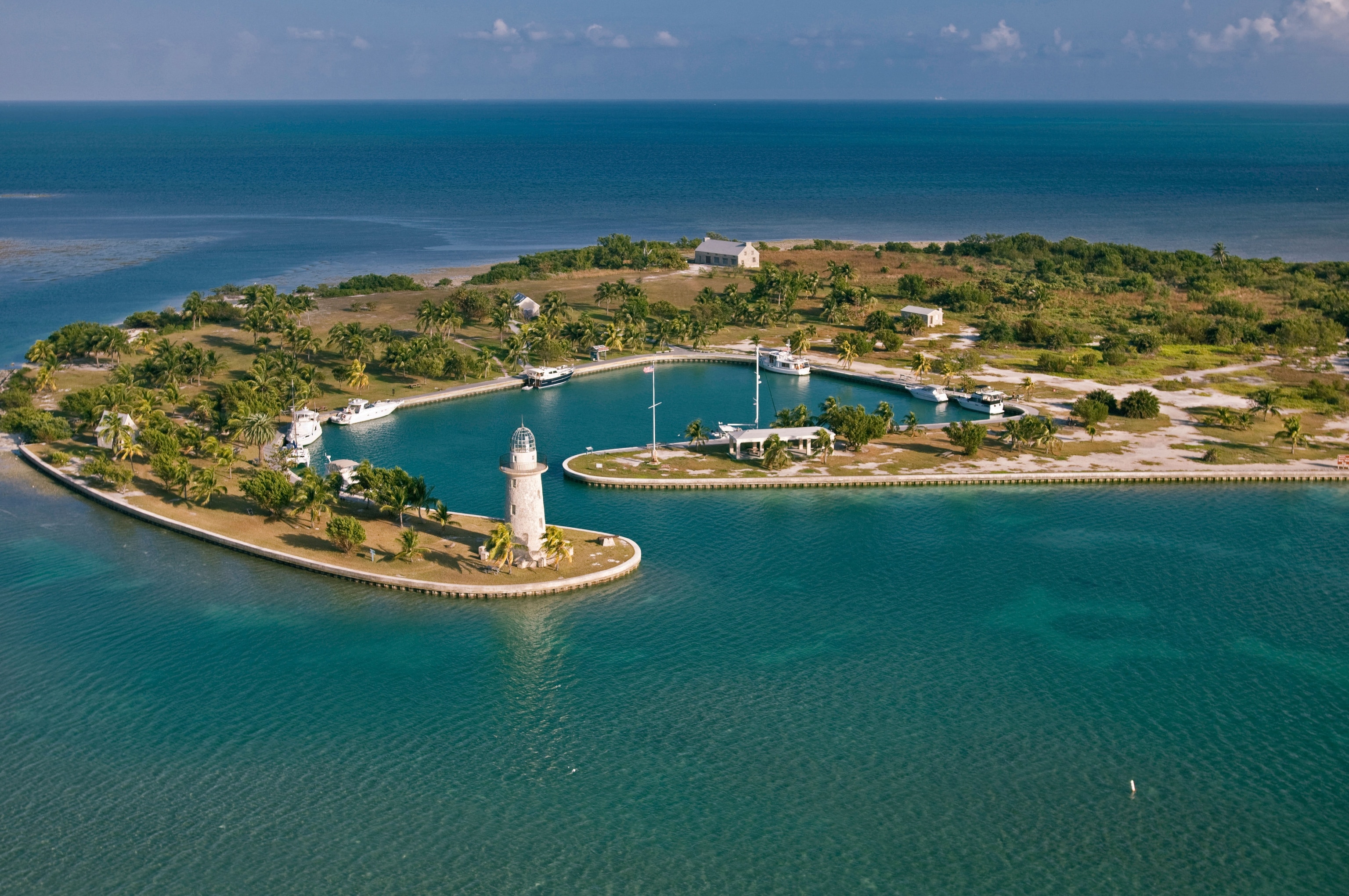 Tropical landmass surrounded by water, boats docked on the edges, lighthouse at the tip of the island