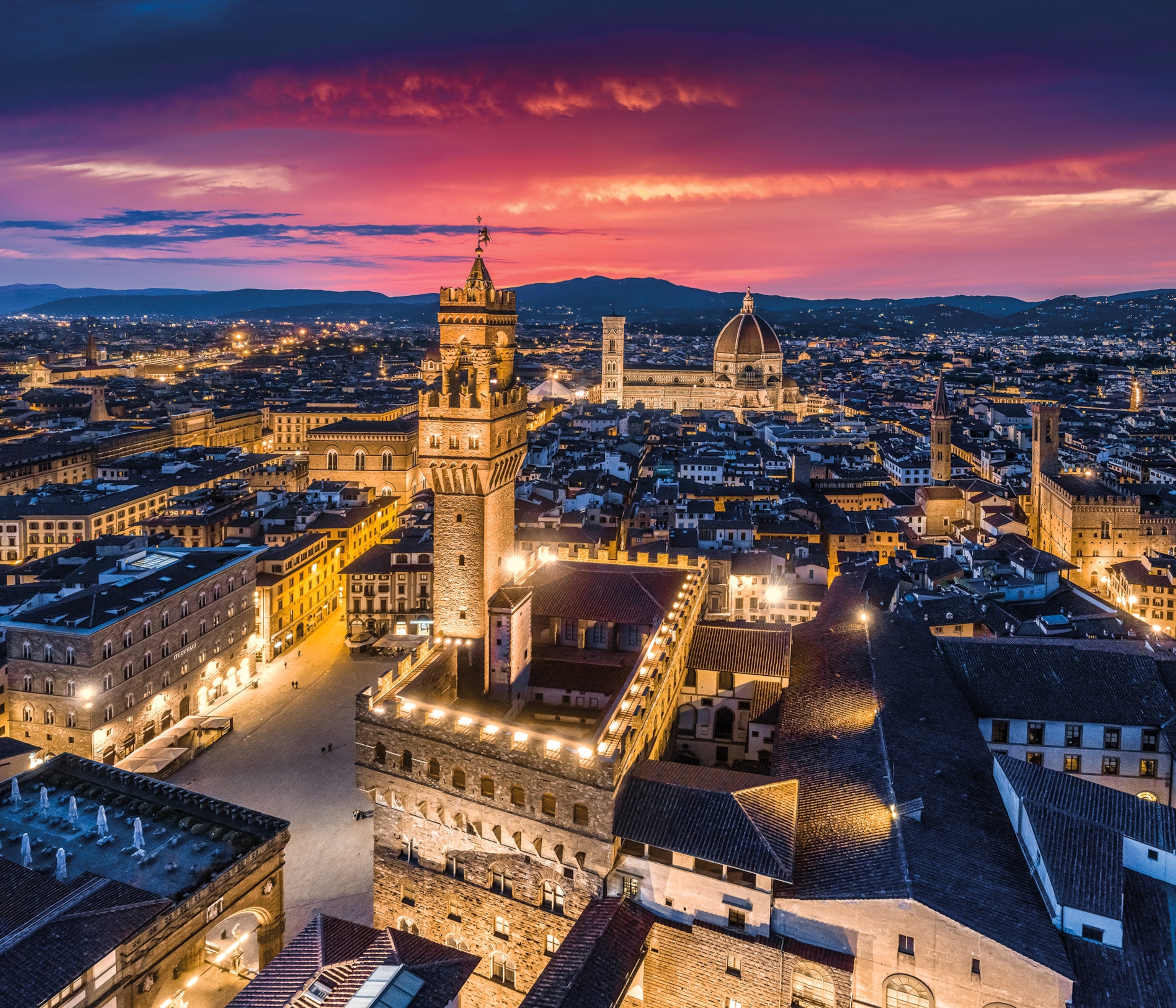 Palazzo Vecchio, a central plaza, is lit up at night with the Duomo in the background