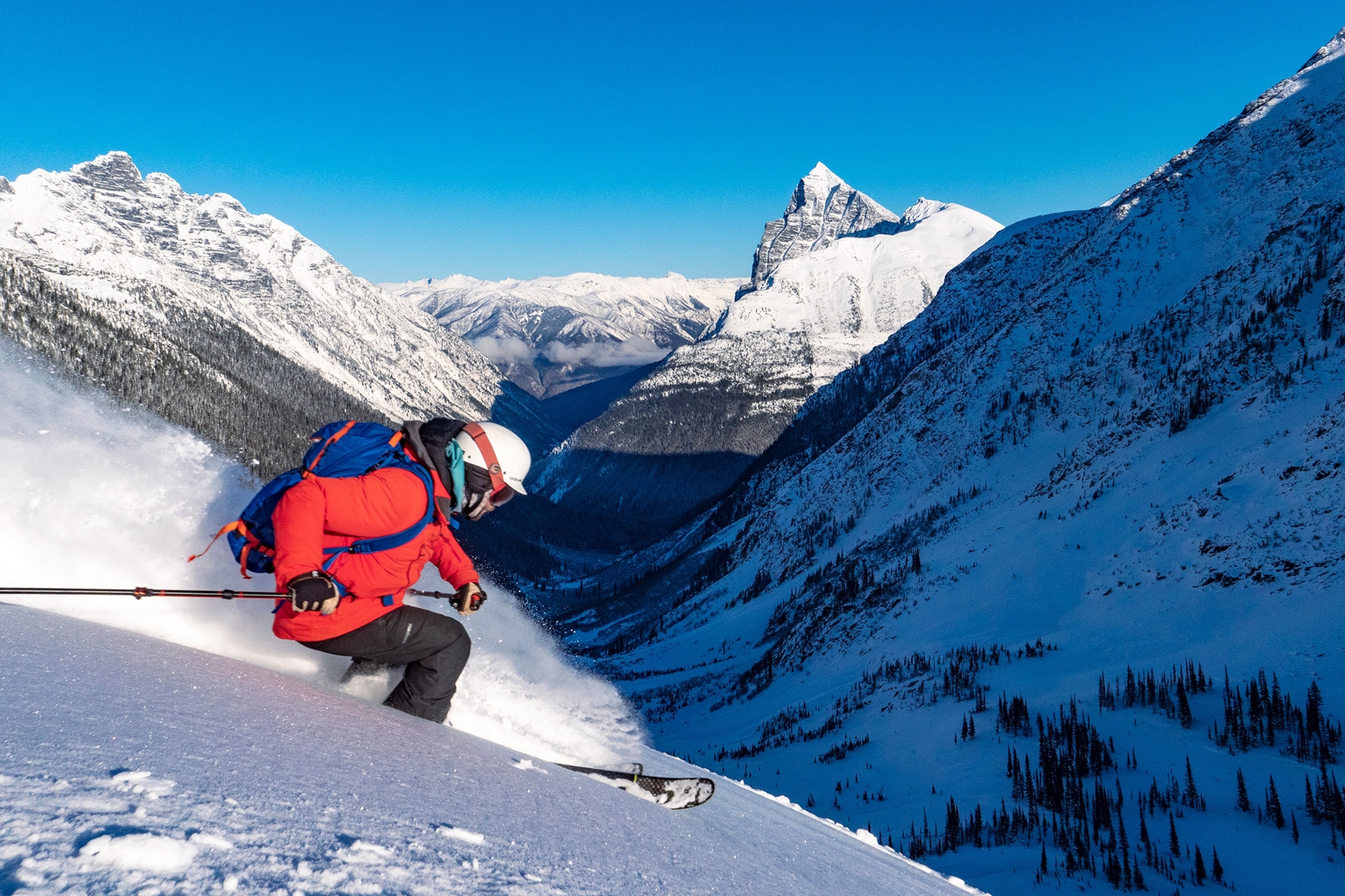 A person in a bright red jacket skis down a mountain at Glacier National Park.