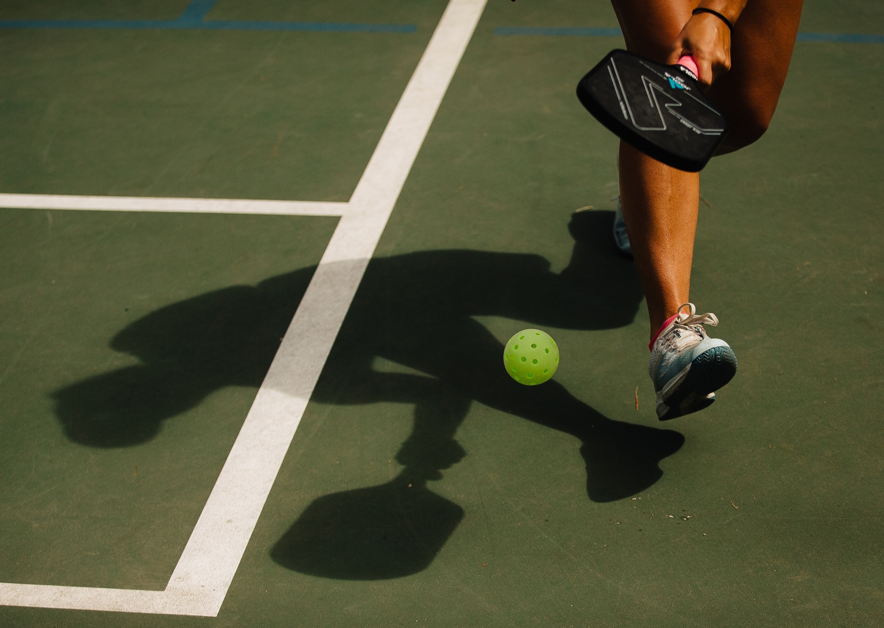The shadow and legs of a pickelballer chasing down a ball during a match.