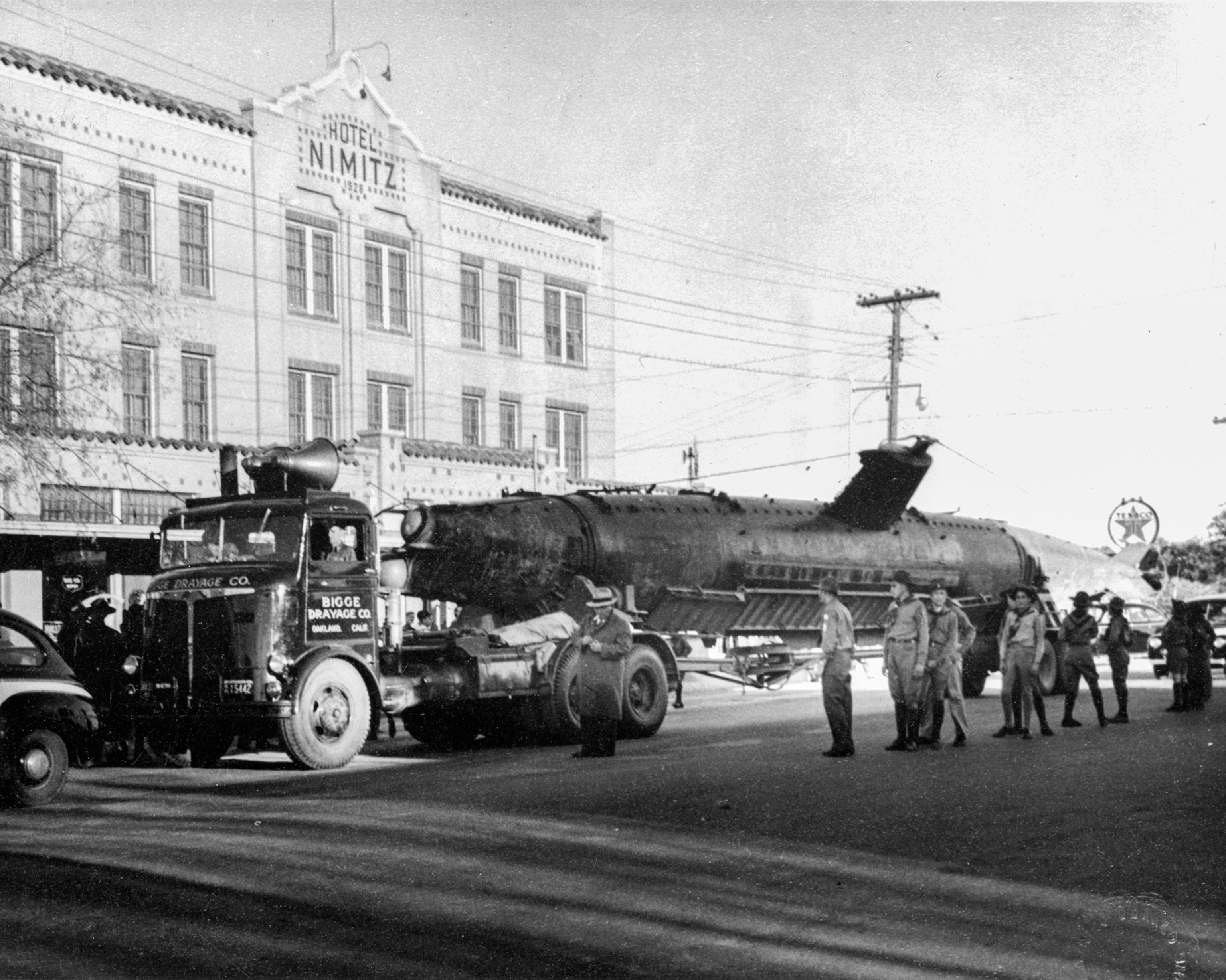 a black and white photo of a submarine on the back of a truck driving down a street in 1943