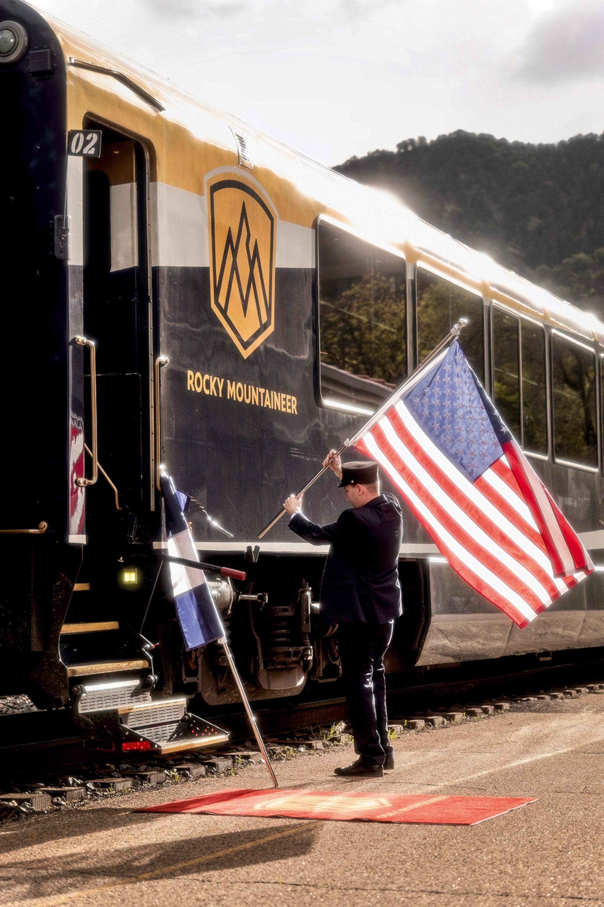 A train conductor on a platform, waving the American flag by a shiny train.