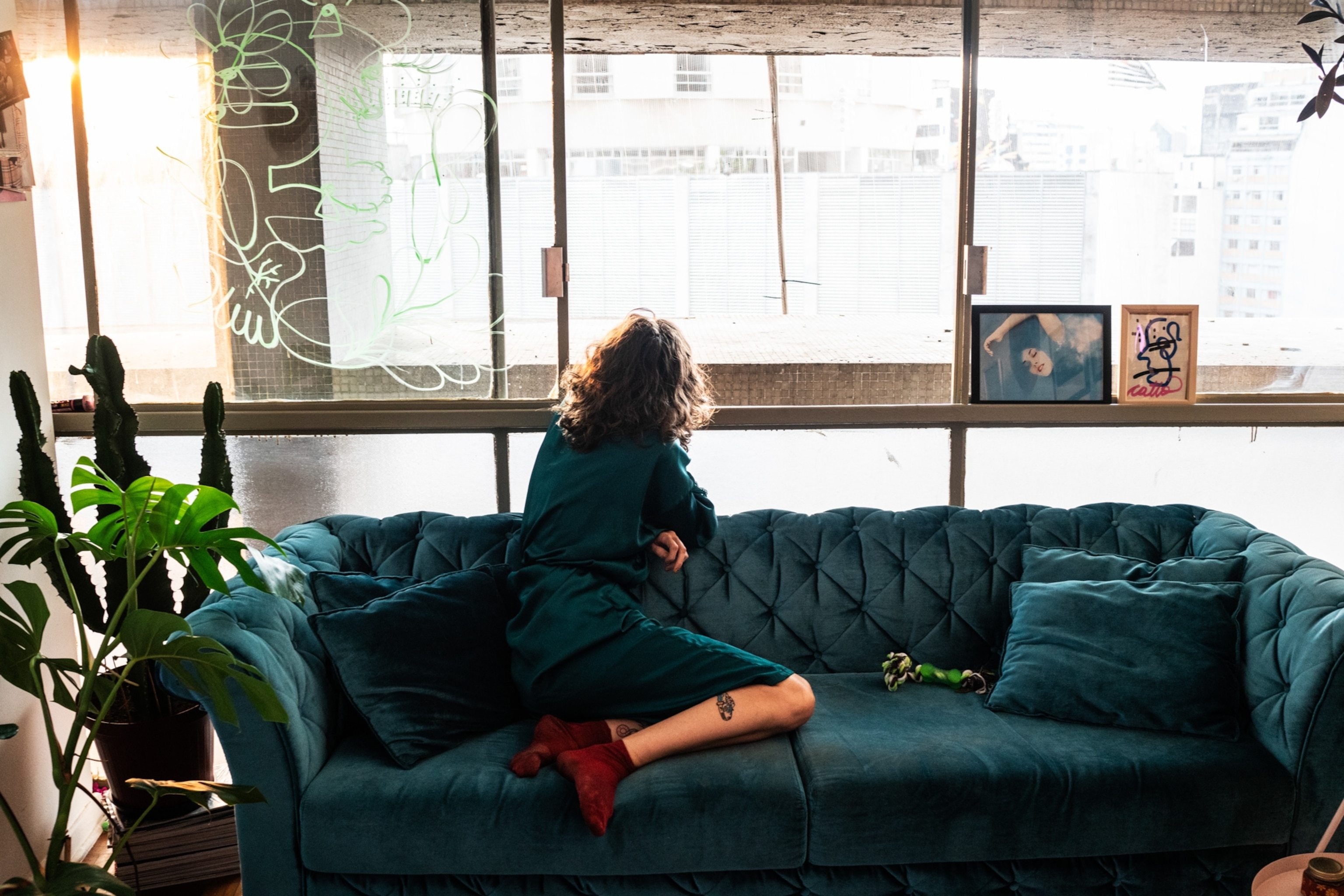 a woman wearing a green dress sitting on a matching green couch looking out of the window