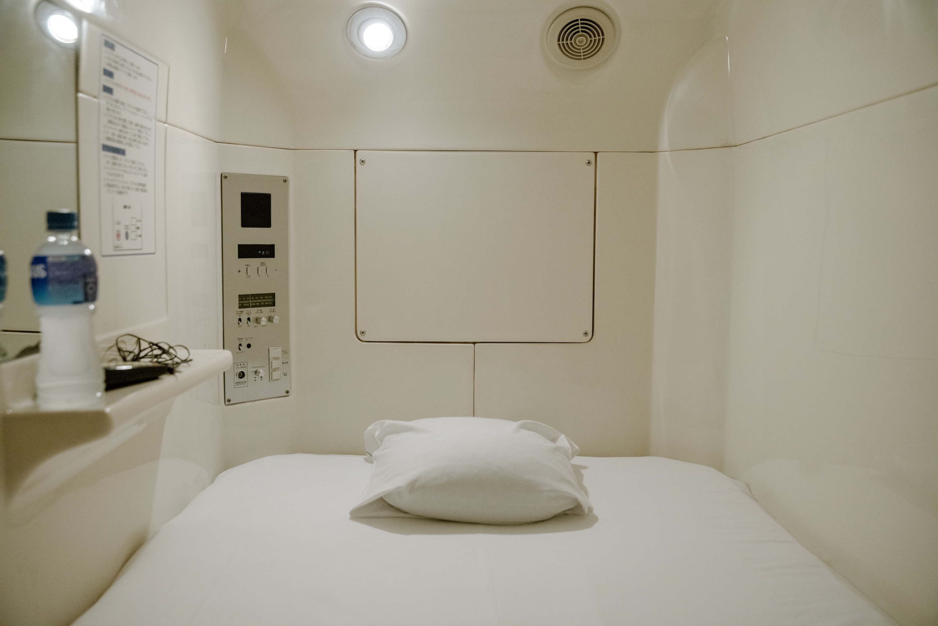 a pillow inside a capsule bed, on the ledge in the capsule there is a water bottle