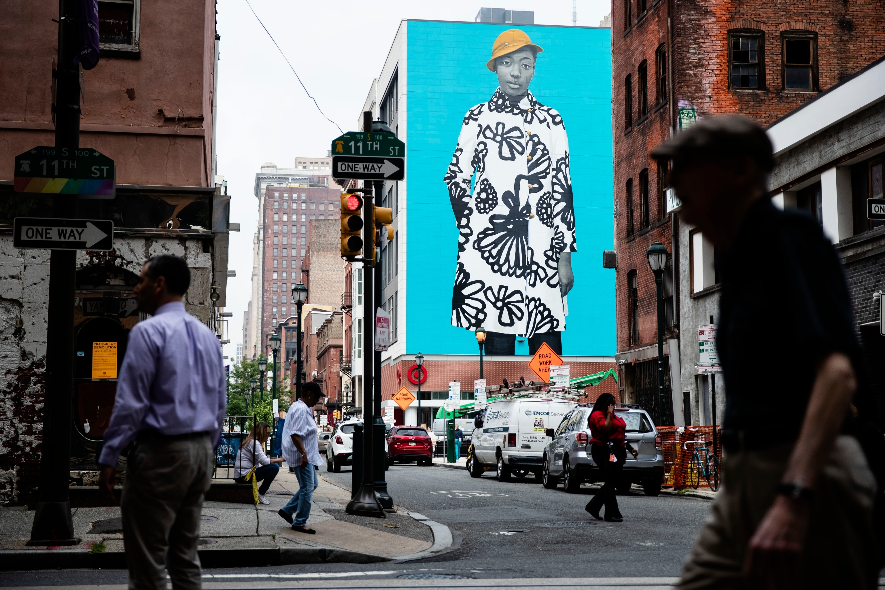 pedestrians walk near a Mural Arts Philadelphia mural of Najee Spencer-Young by artist Amy Sherald
