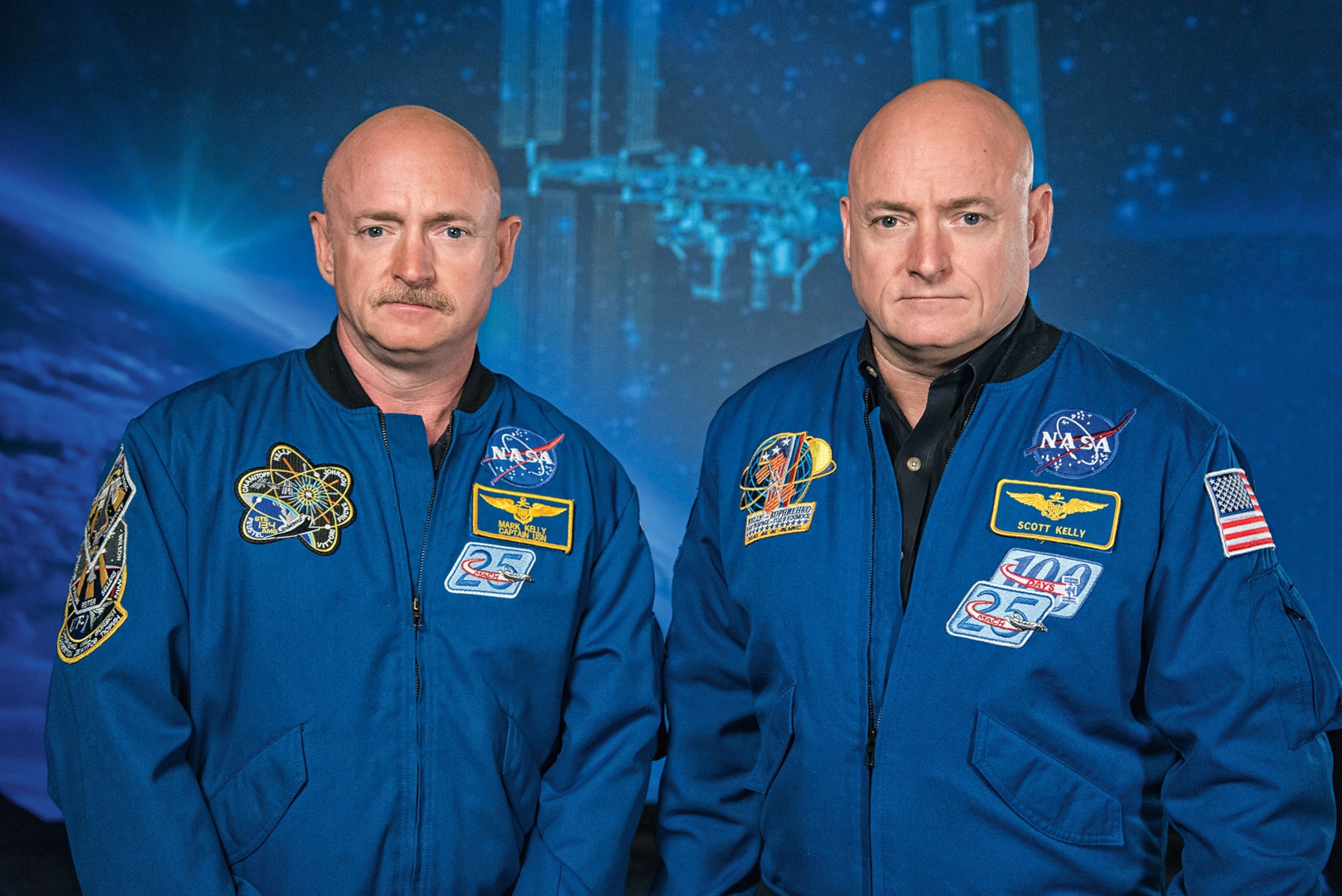 Twins stand on a blue background with nasa logos and branding on their jacket.