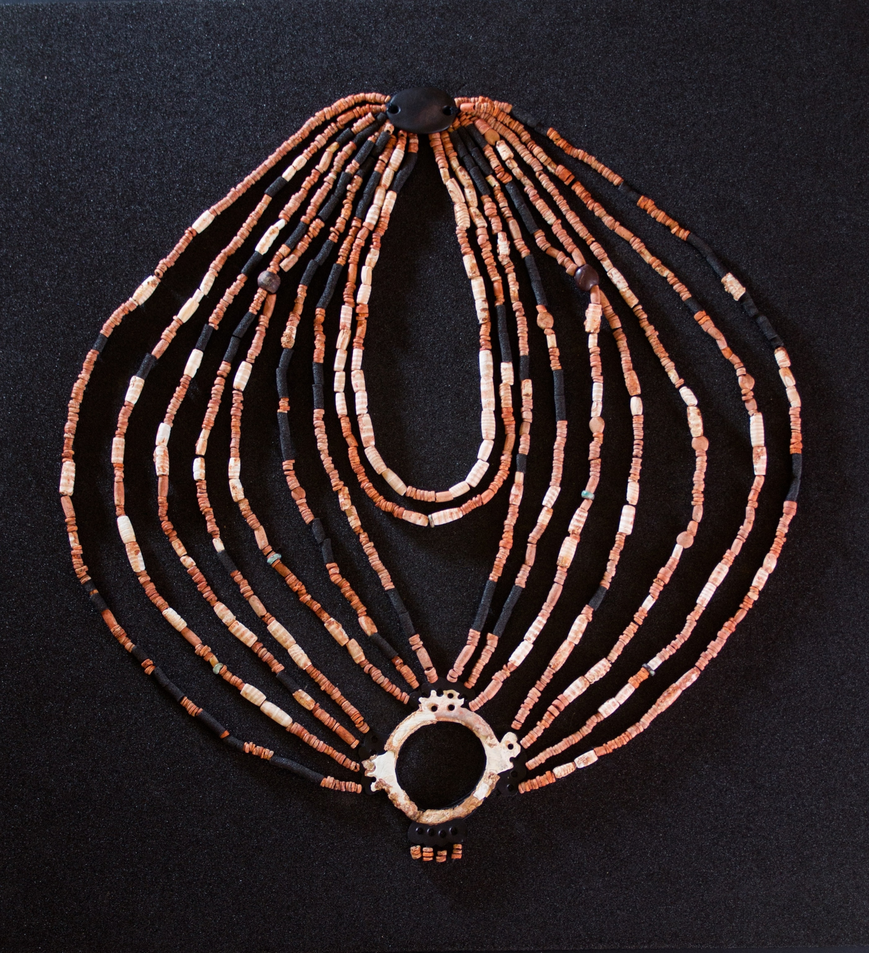 A brown and white and black necklace sits on a black foam, the black pieces that would be calcite beads have been subbed for foam to aid in the reconstruction.