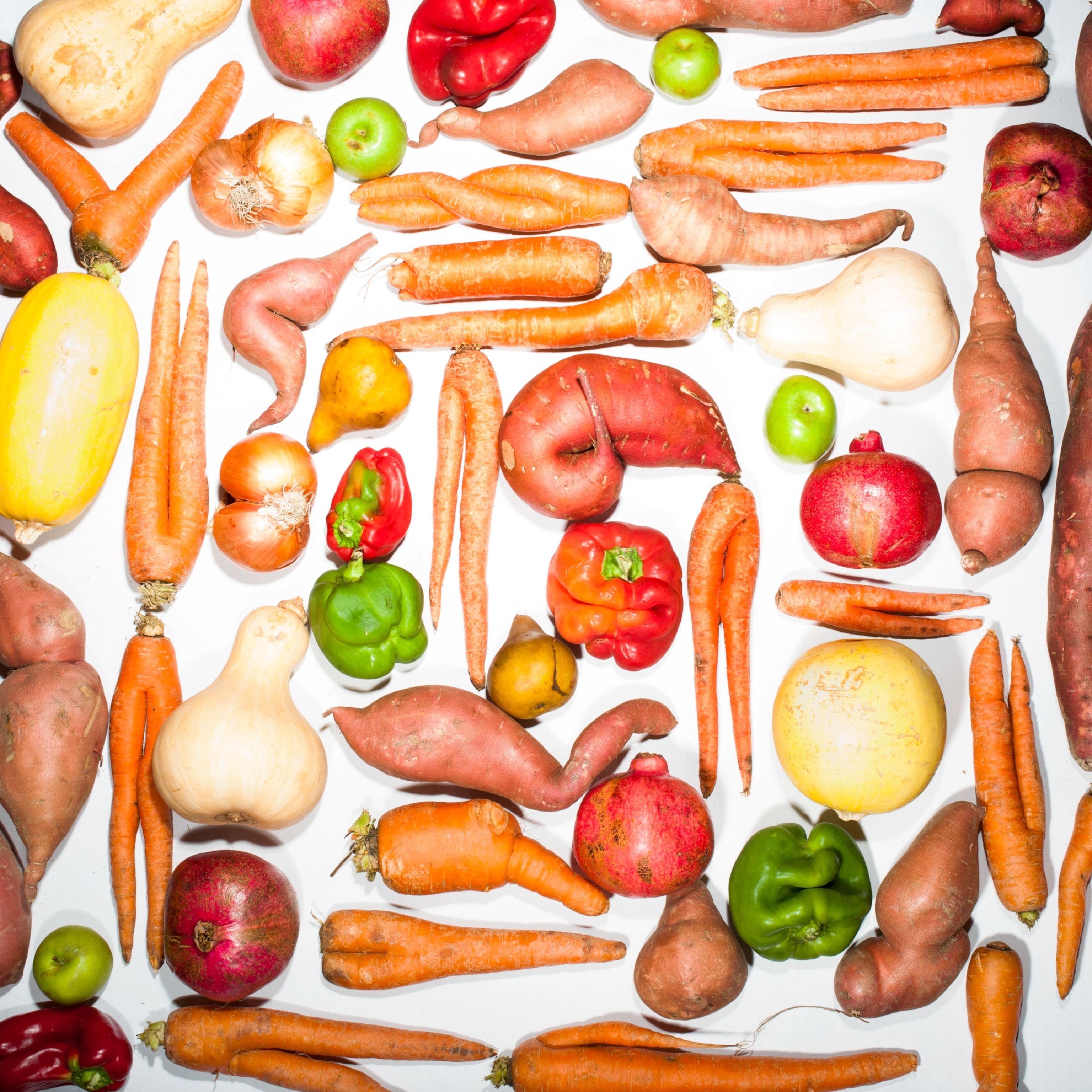 Dozens of imperfect produce such as carrots with twisted stalks and irregularly shaped bell peppers, photographed against a white background.