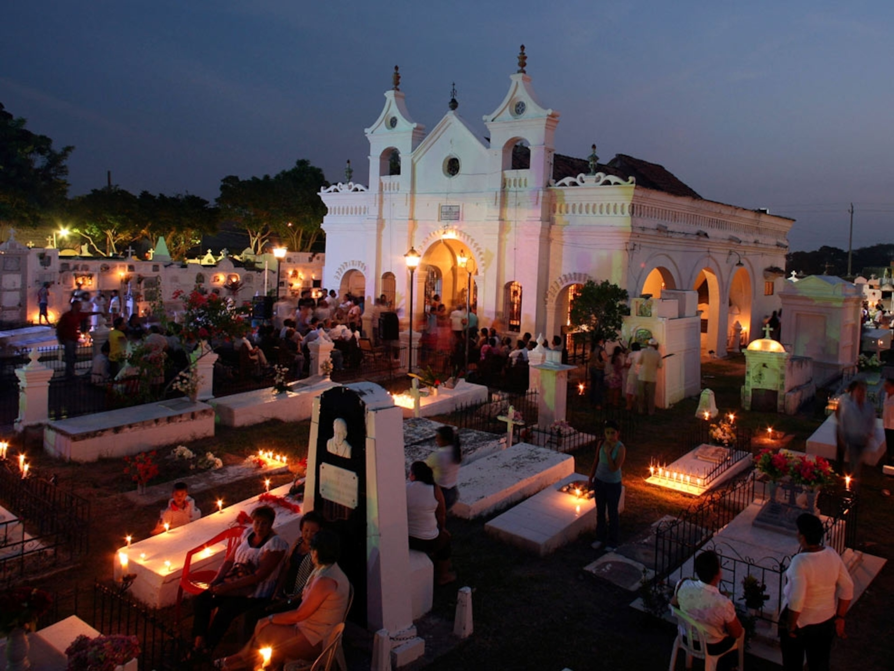 People visiting graves in candle-lit cemetery