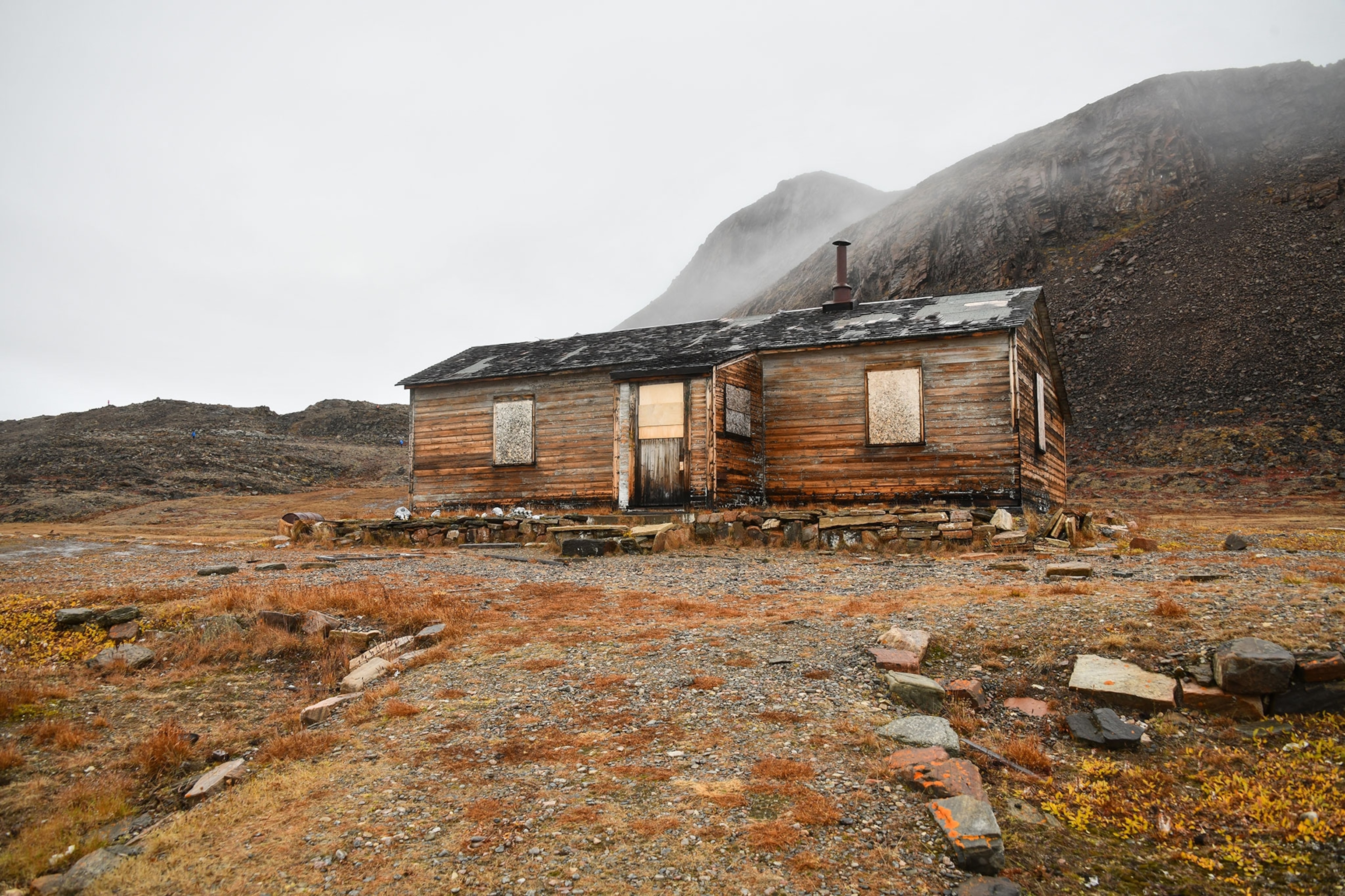 A boarded up abandoned building sits at the bottom of a hillside on a foggy day.