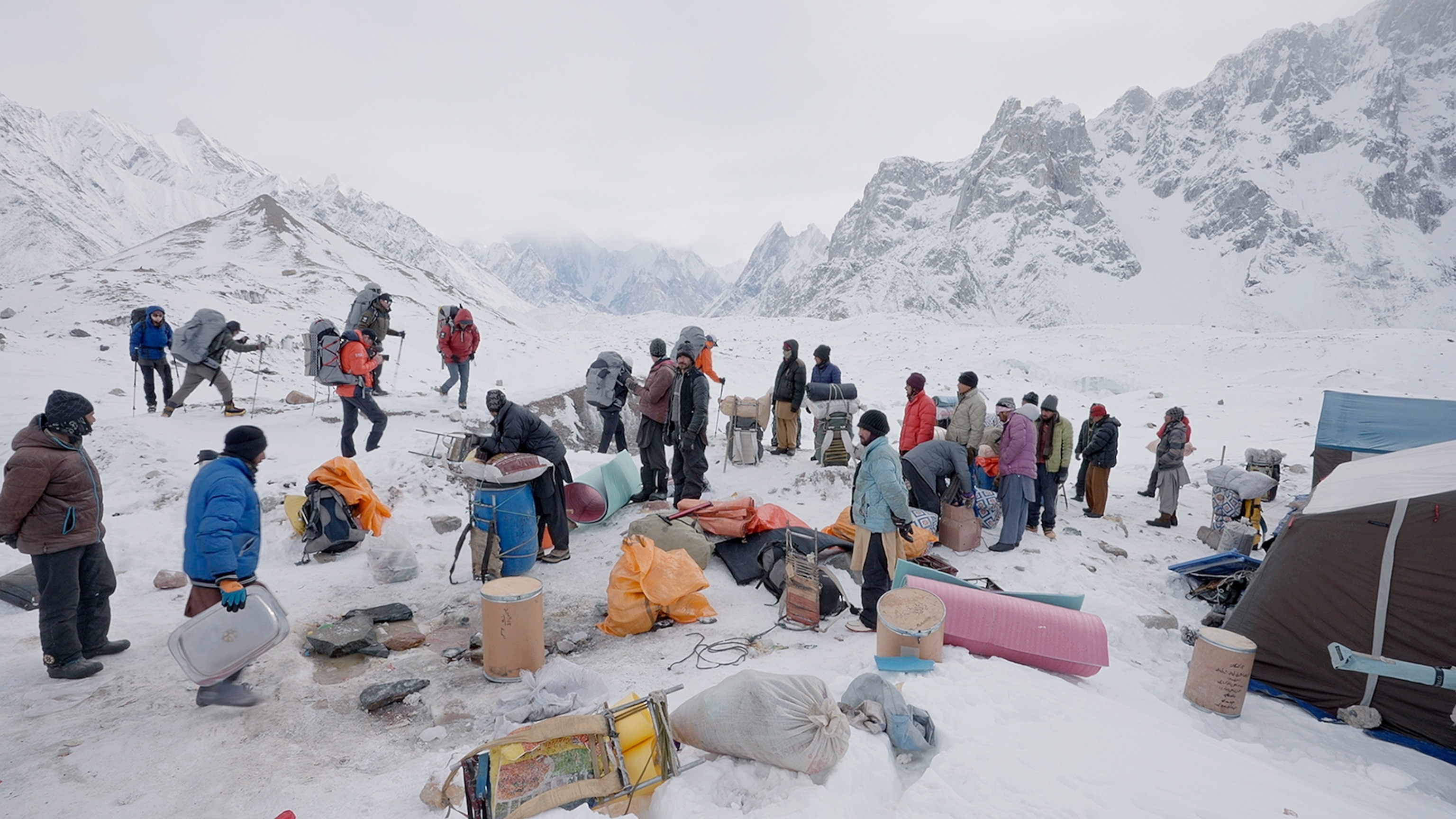 Picture of mountain camp full of gears and people on grey day.