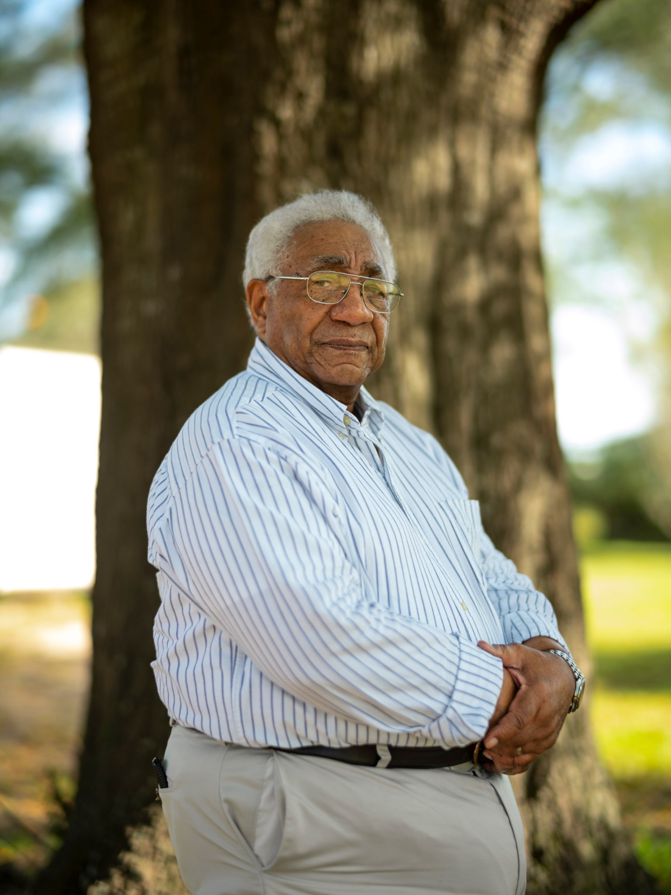 a man in a striped button down shirt standing in front of a tree