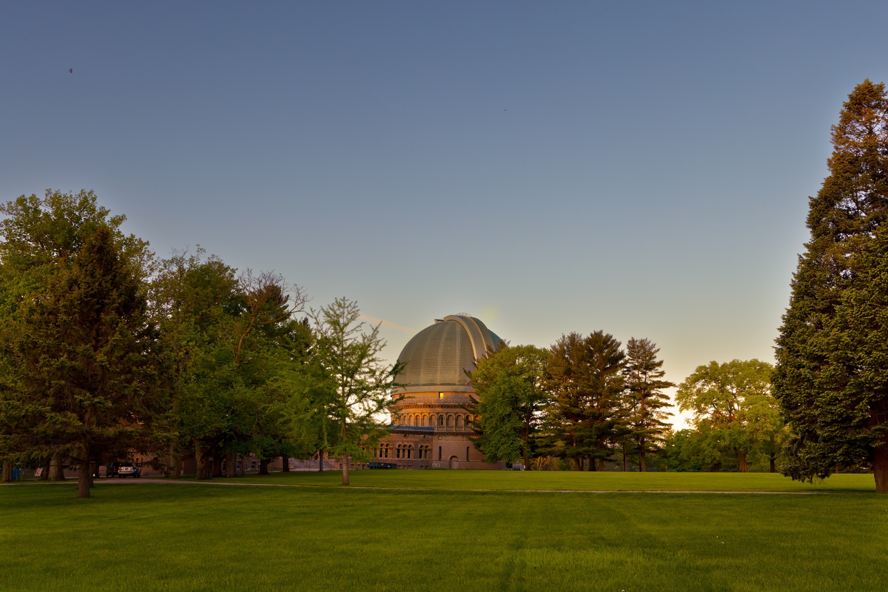 Sunrise behind observatory and perfectly green lawn in front of it surrounded by trees.