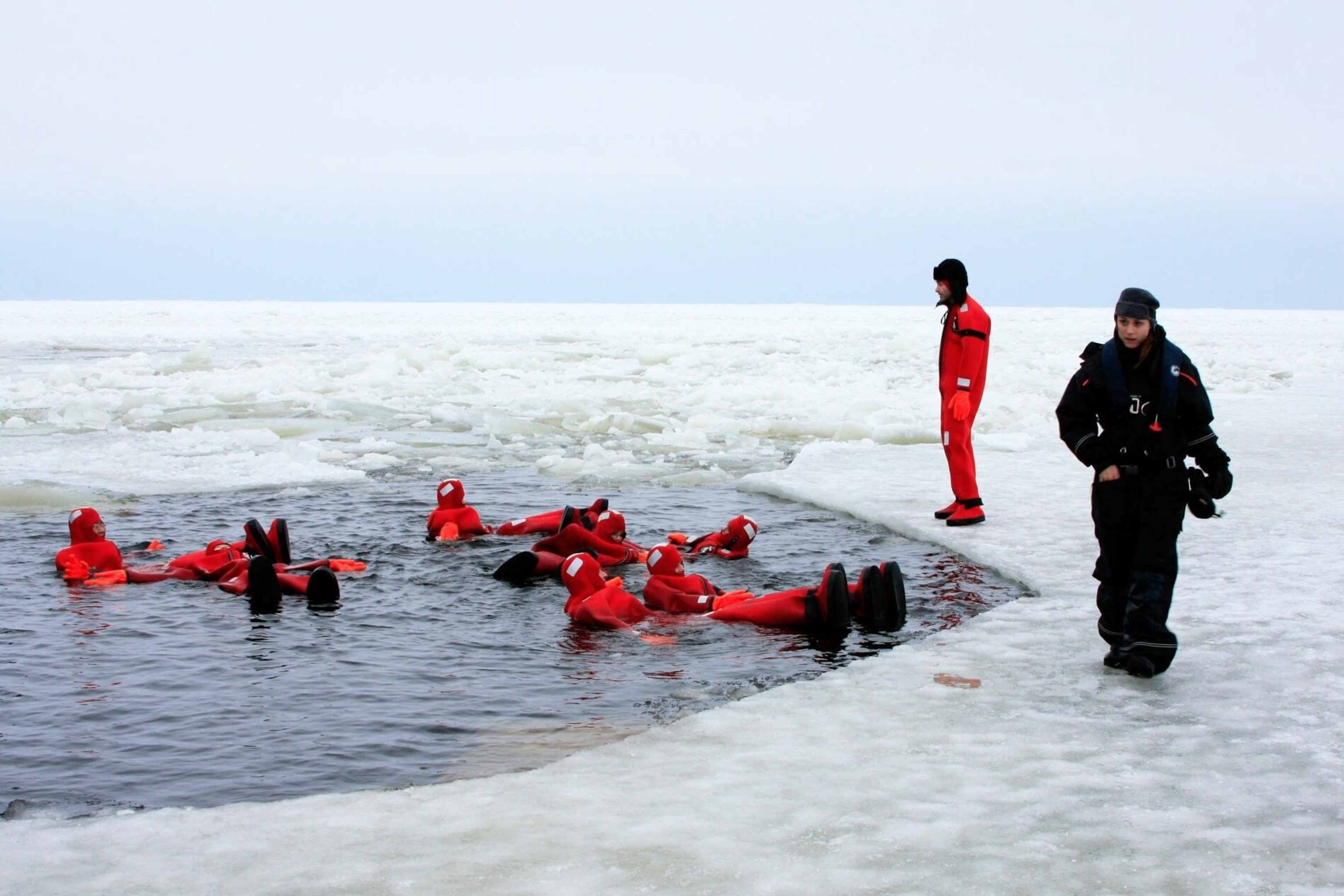 People floating in a frozen lake in orange rubber suits.
