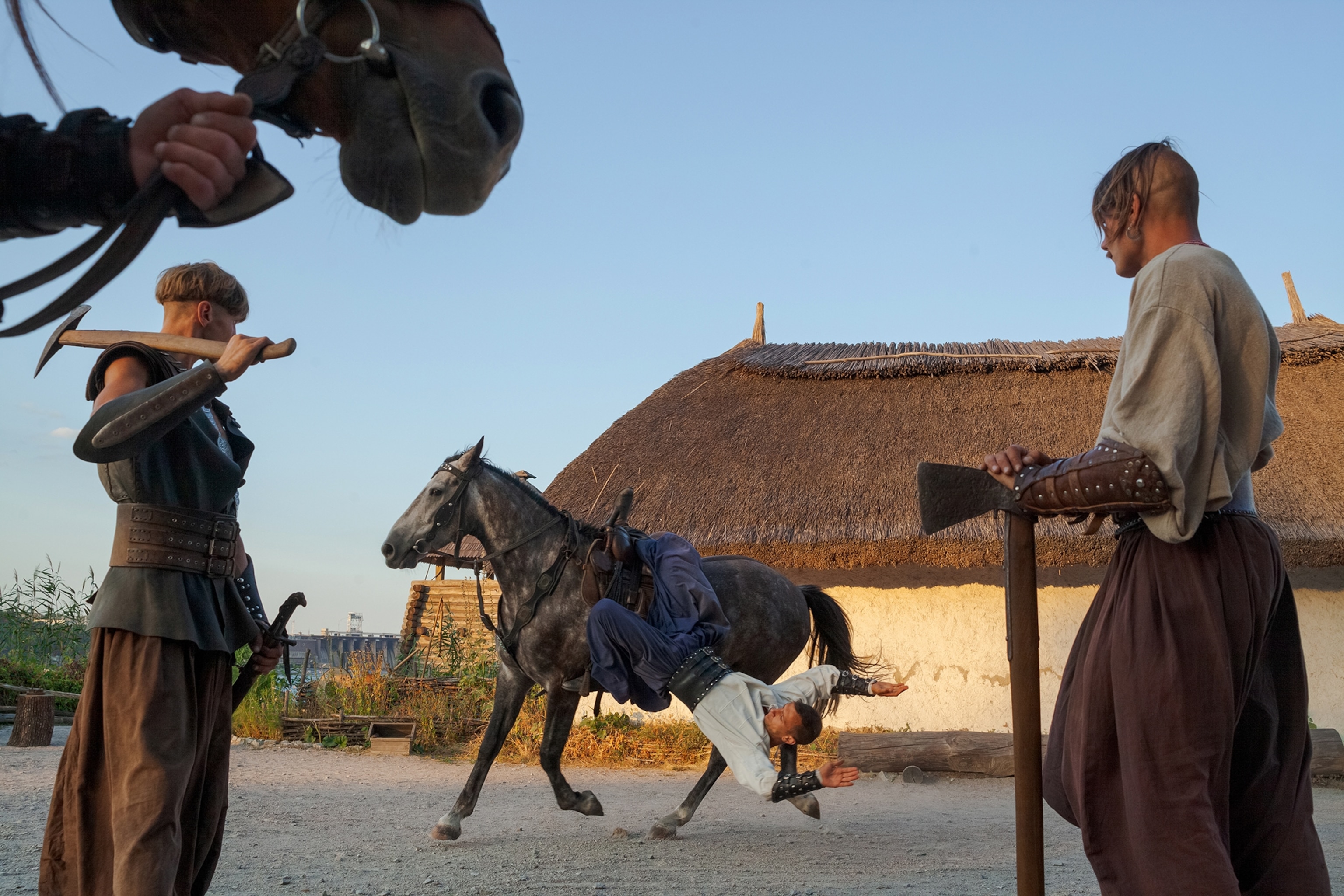two cossacks watching another one doing acrobatics on horseback.
