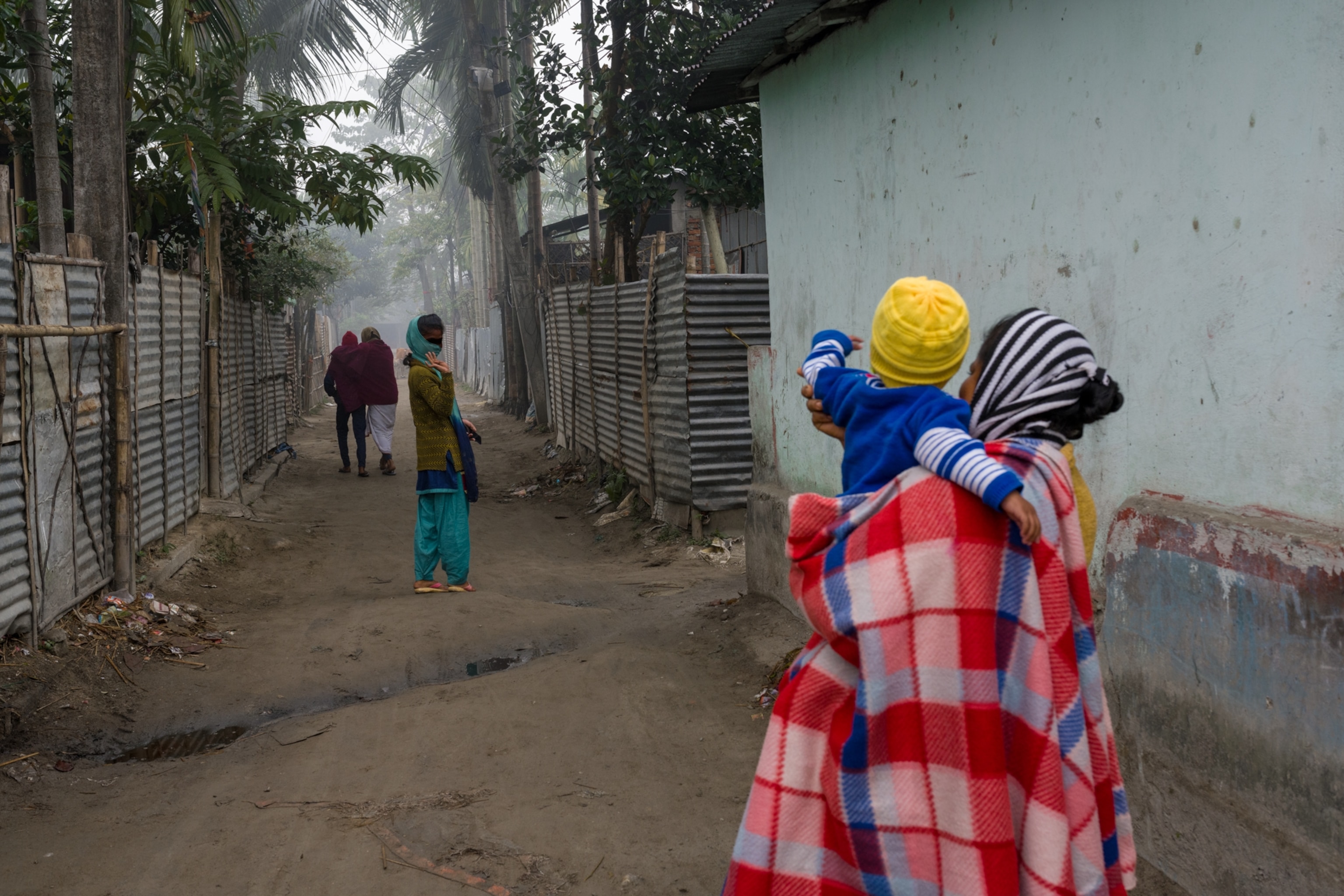 a woman walking down the street waving back at a mother holding a baby