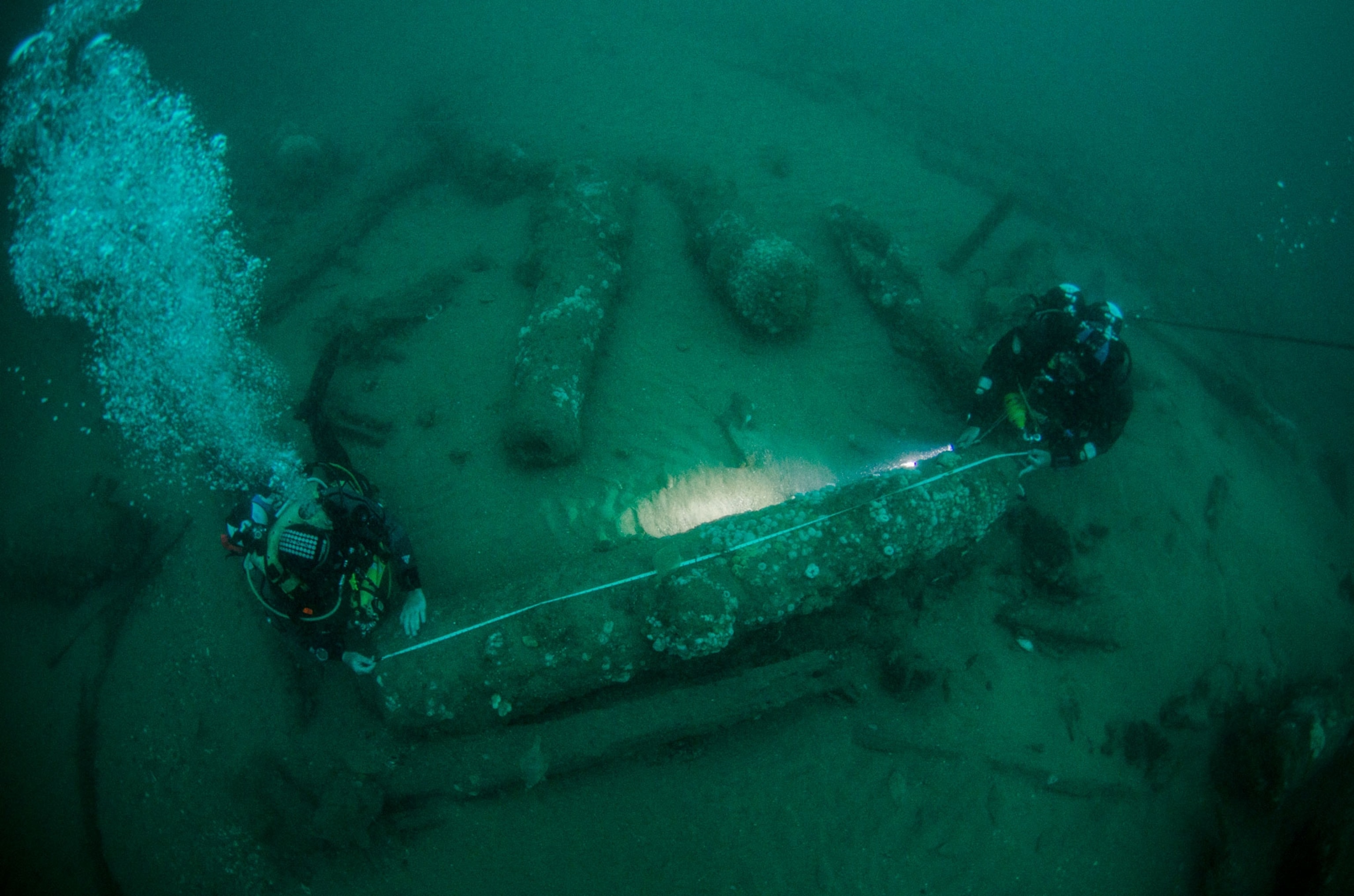 men measuring cannons on a shipwreck in England
