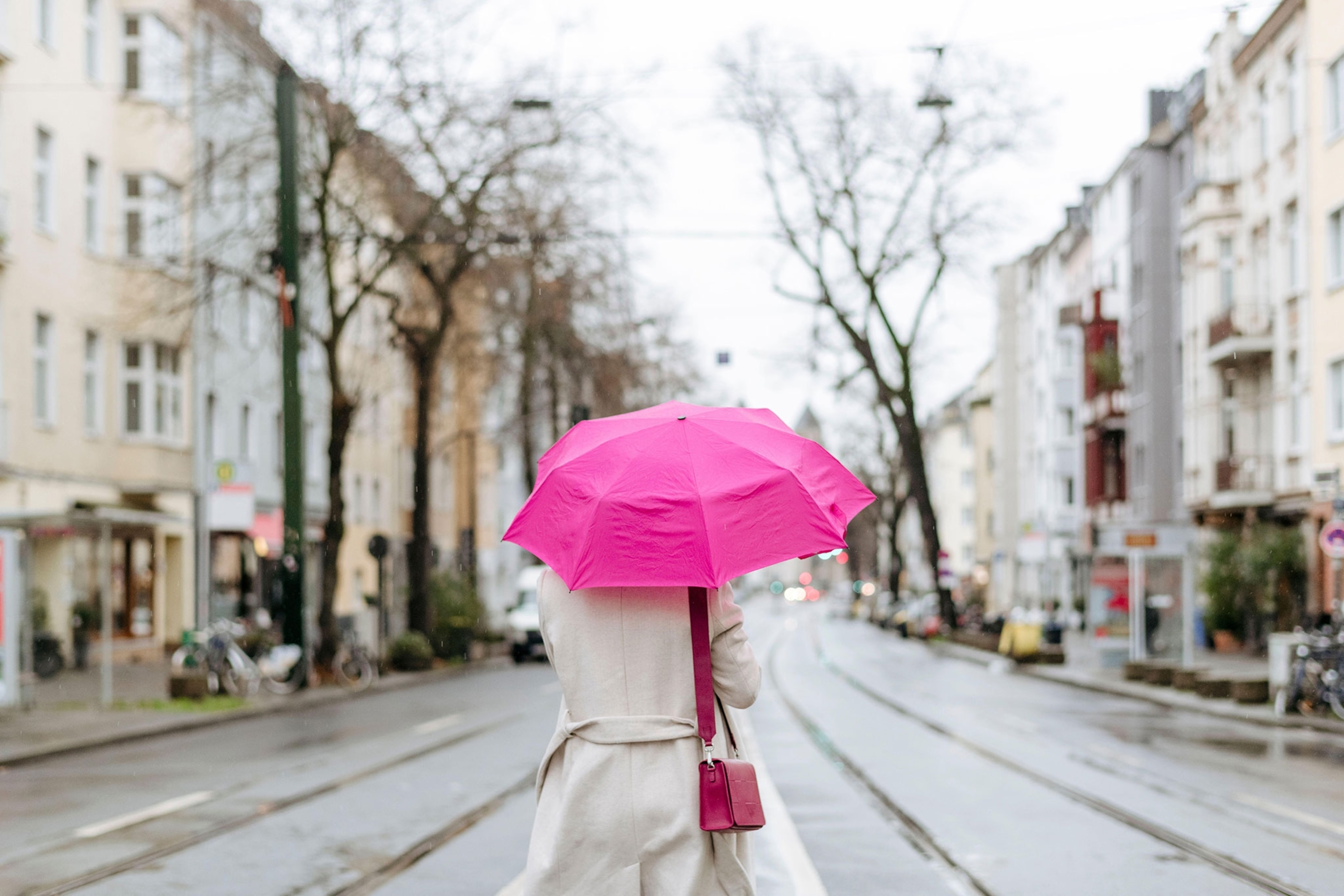 Person walking down city street with pink umbrella.