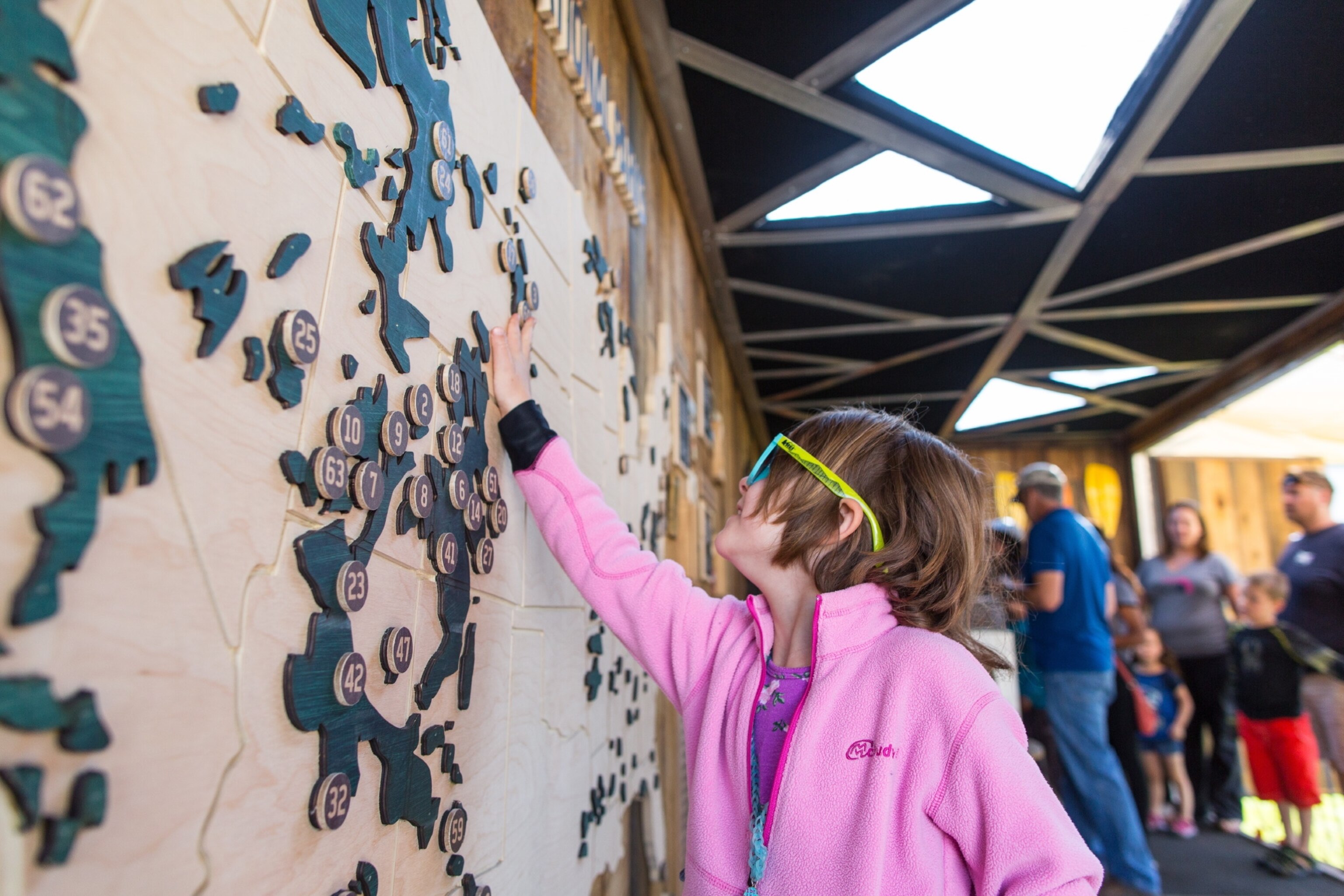 A young girl in a pink sweater pointing to a map