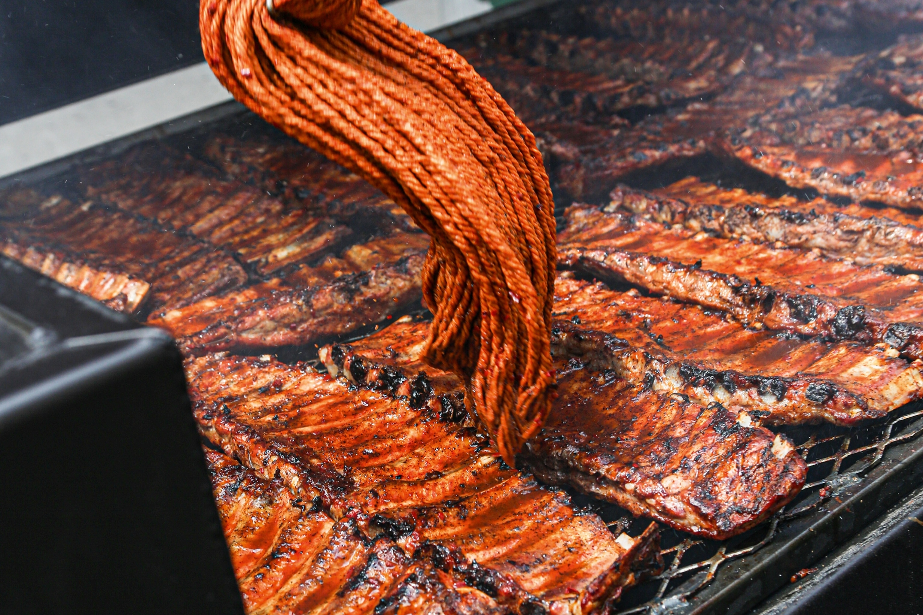 Mopping sauce onto ribs on a grill at Whole Hog BBQ.