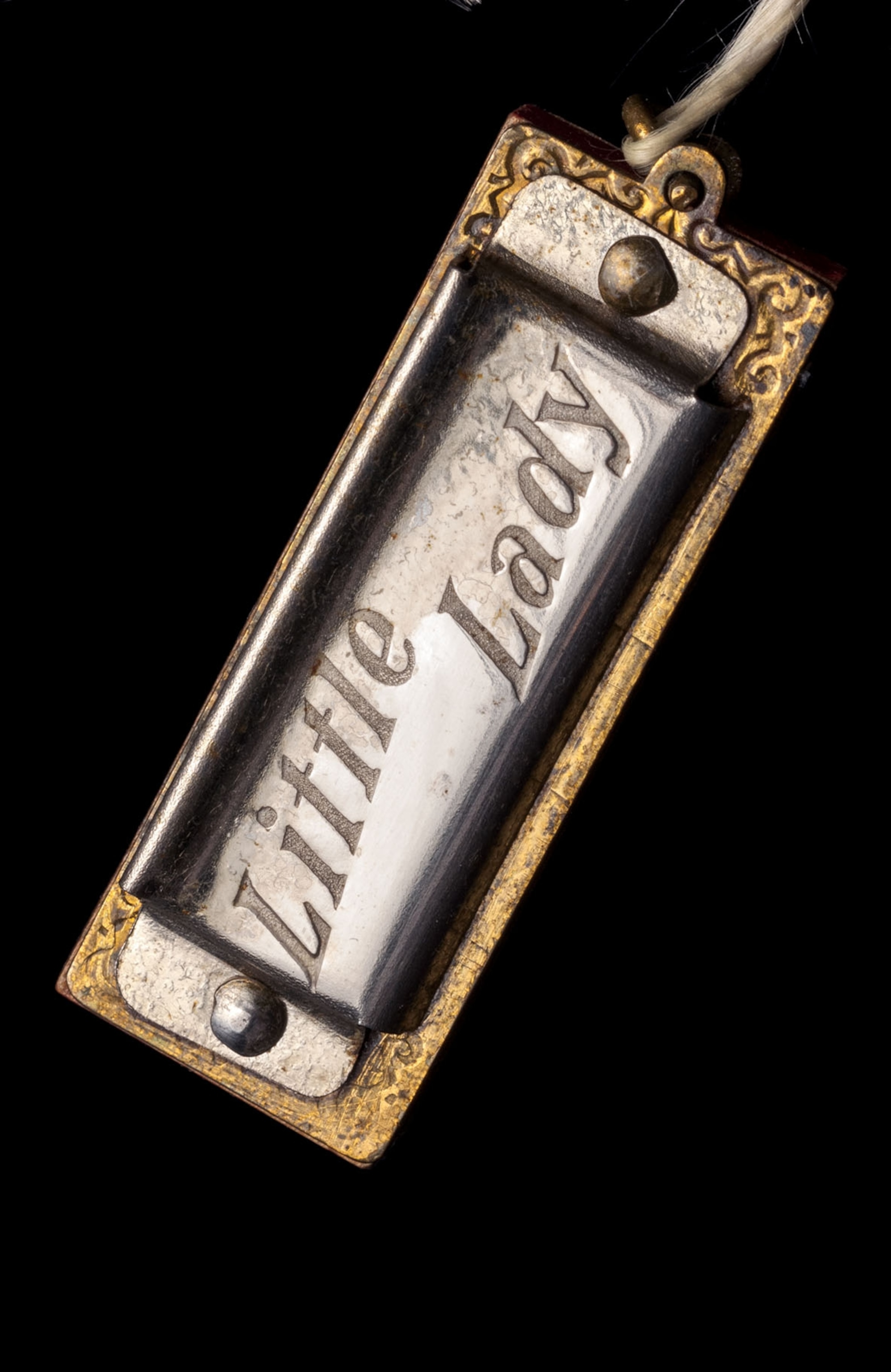 a silver and gold harmonica with "Little Lady" inscribed on black