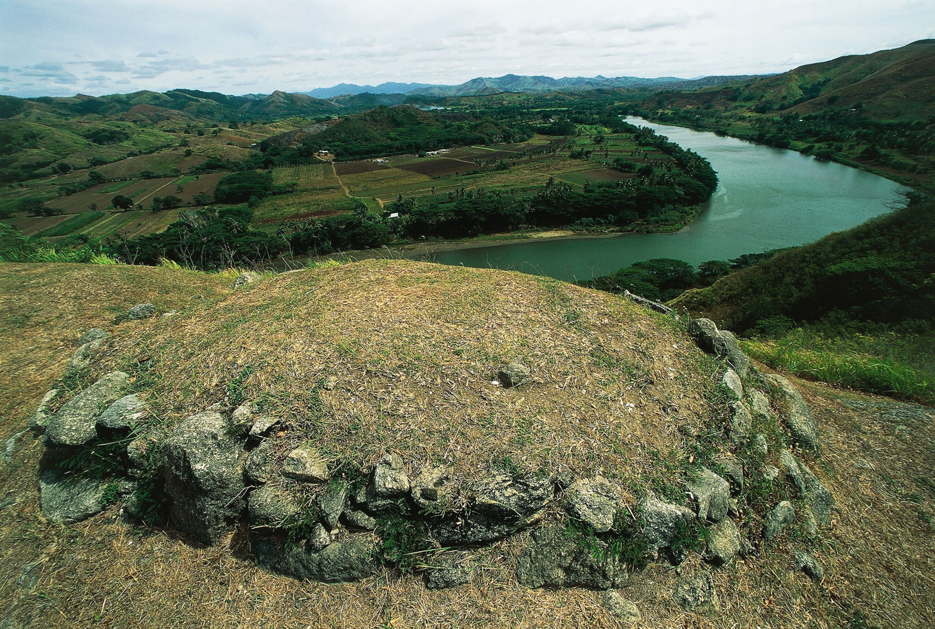 The tomb, a mound of grass with a wall of rocks around it, of the chieftain in Tavuni Hill Fort and the Sigatoka river, Sigatoka Valley, Viti Levu Island, Fiji.