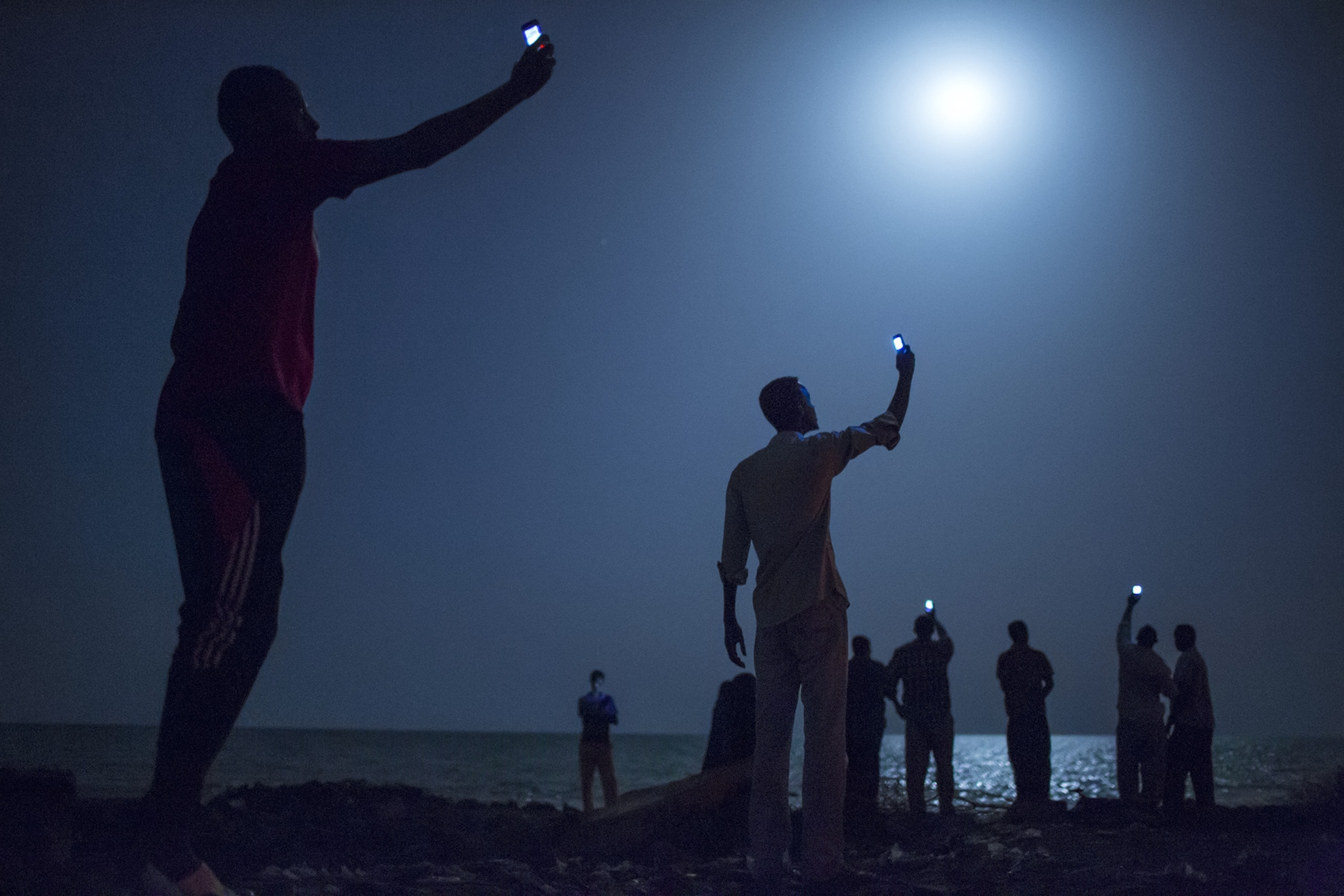A group of people on a beach at night lifting cell phones up above their heads