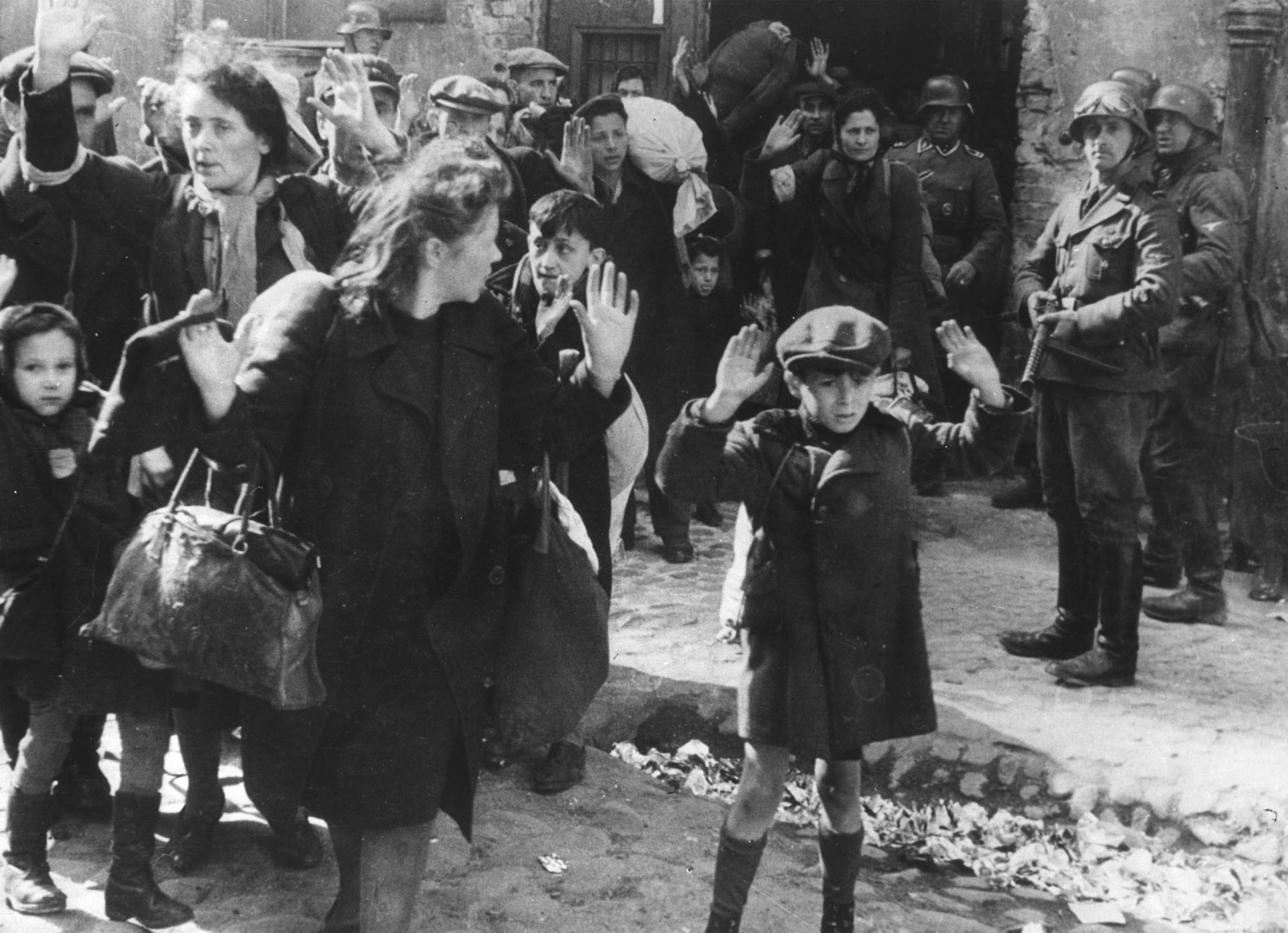 a people being rounded up, a young boy holds up his hands