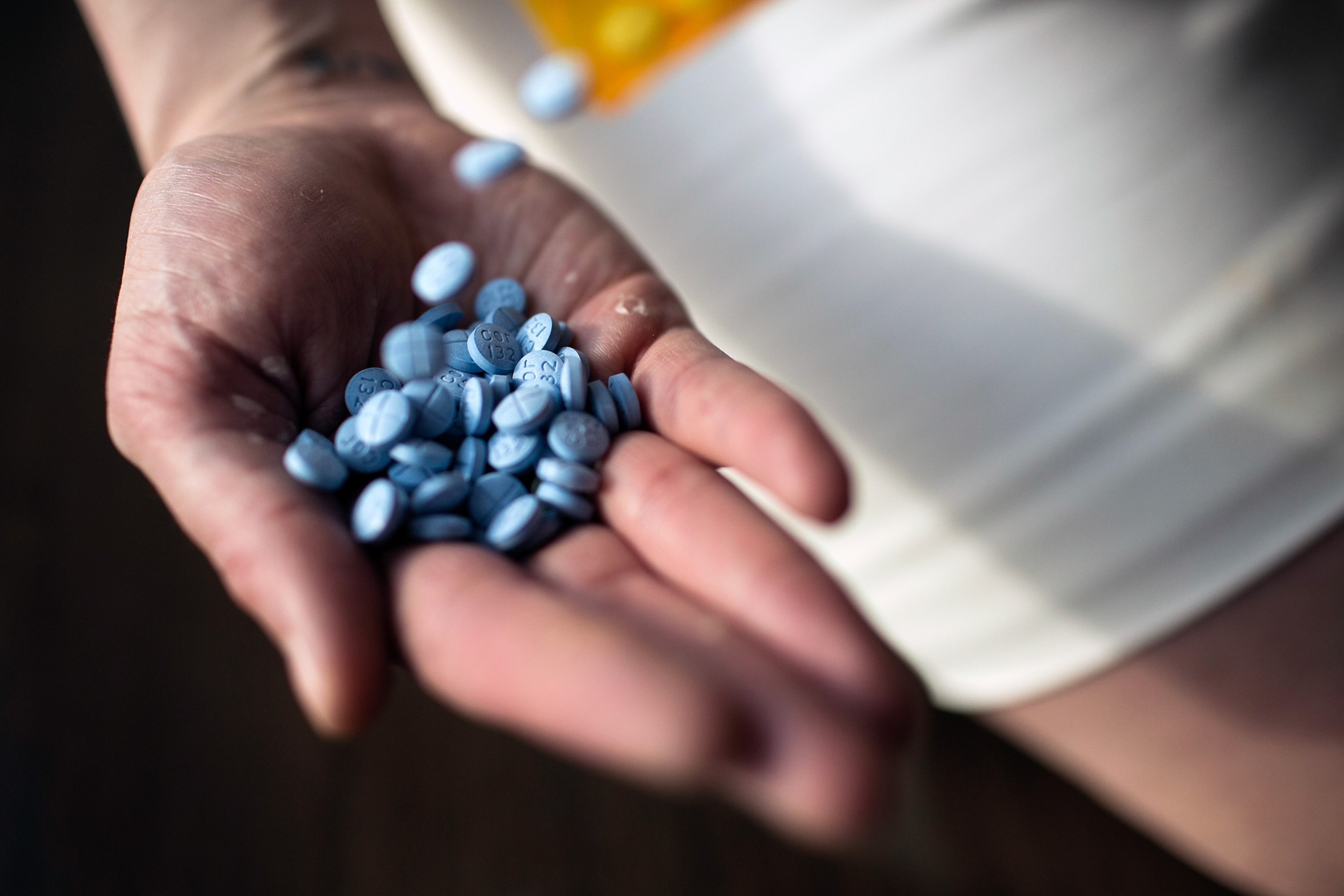A woman pours a bottle of blue Adderall pills into her palm.