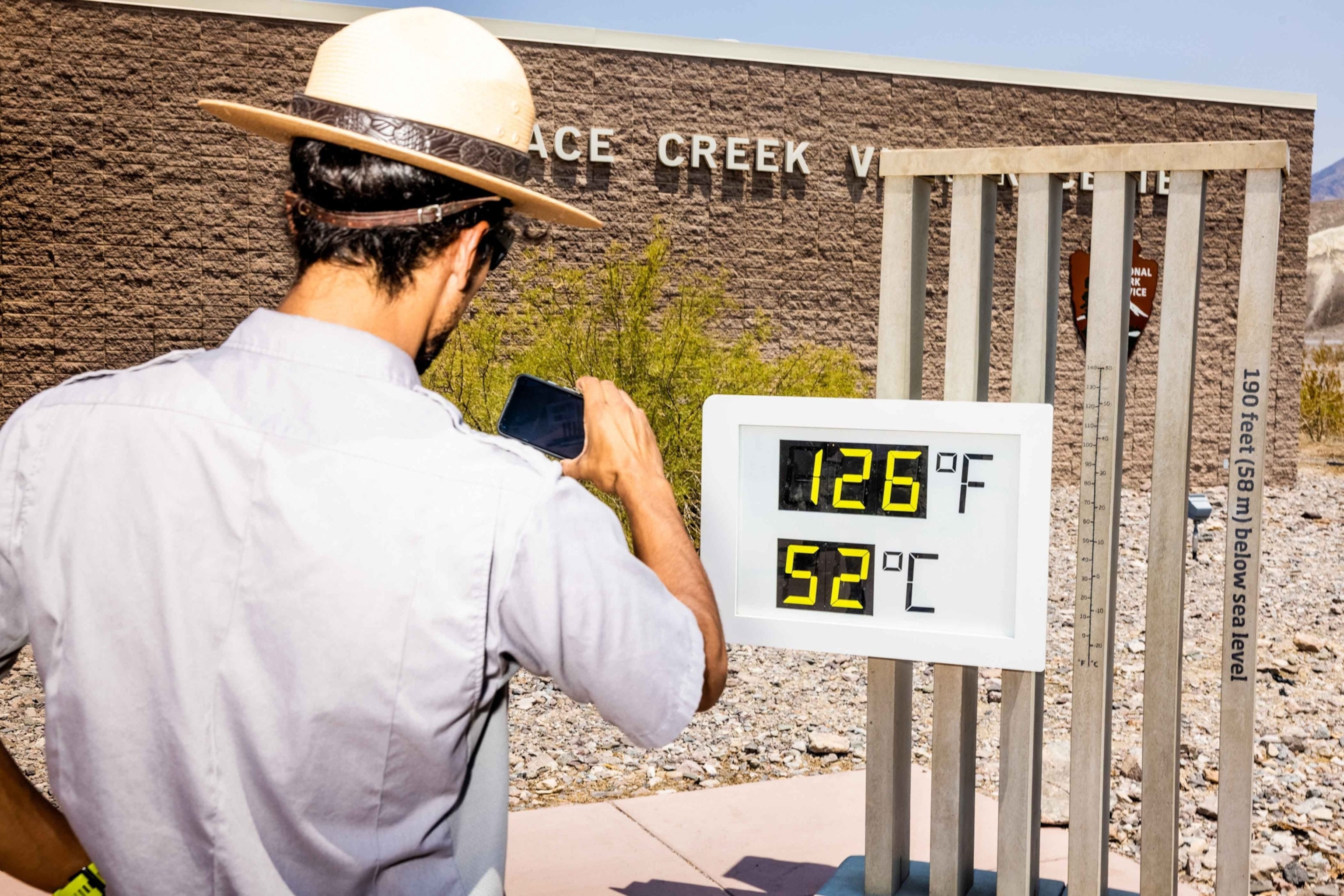 A park ranger taking a photograph of a digital thermometer that shows temperatures are 126 degrees Fahrenheit, or 52 degree Celsius.