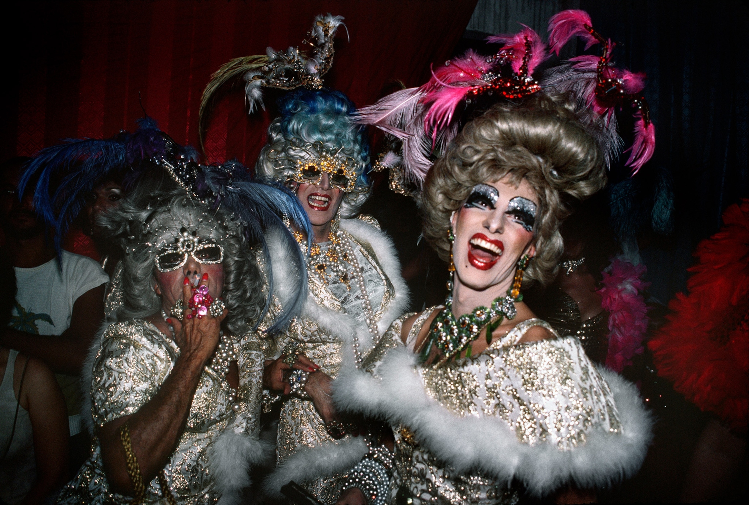 Three people dressed in gowns a with large wigs and lots of color.