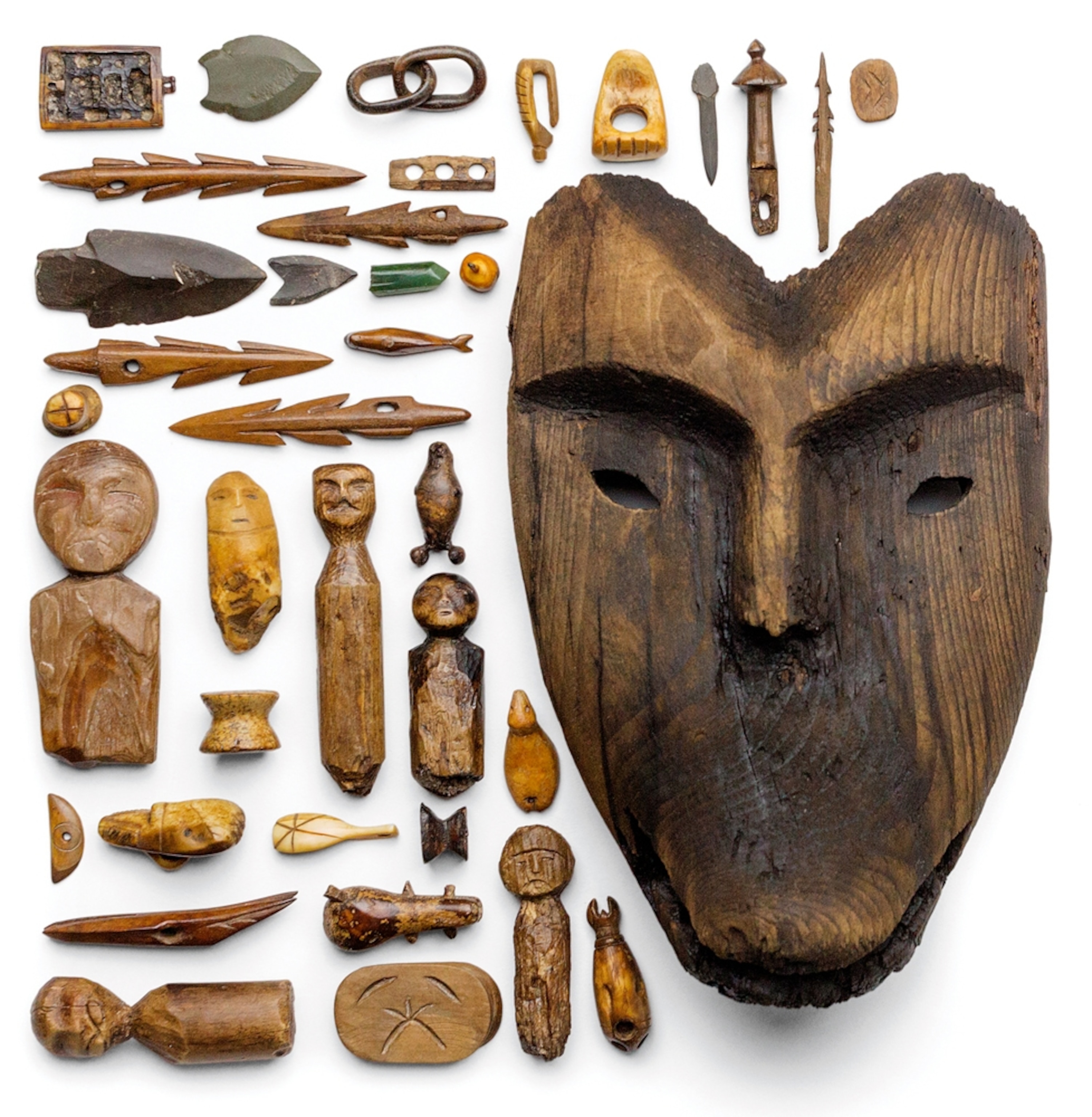 Picture of artifacts made of wood and bones around large wooden human mask.