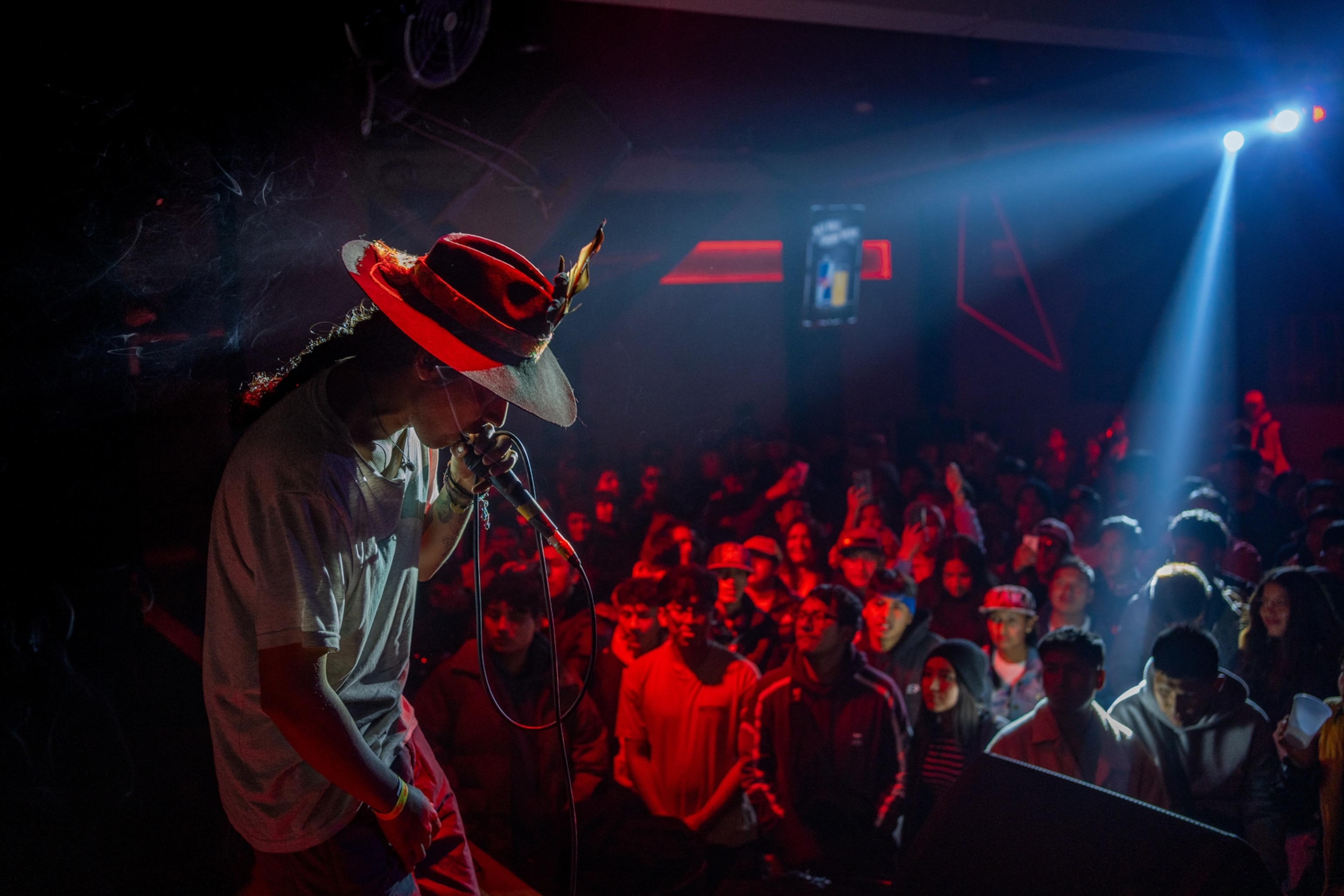 Side profile image of rapper Sara Kutay on stage. The lighting is red. The crowd is seen, slightly blurred, in the background.