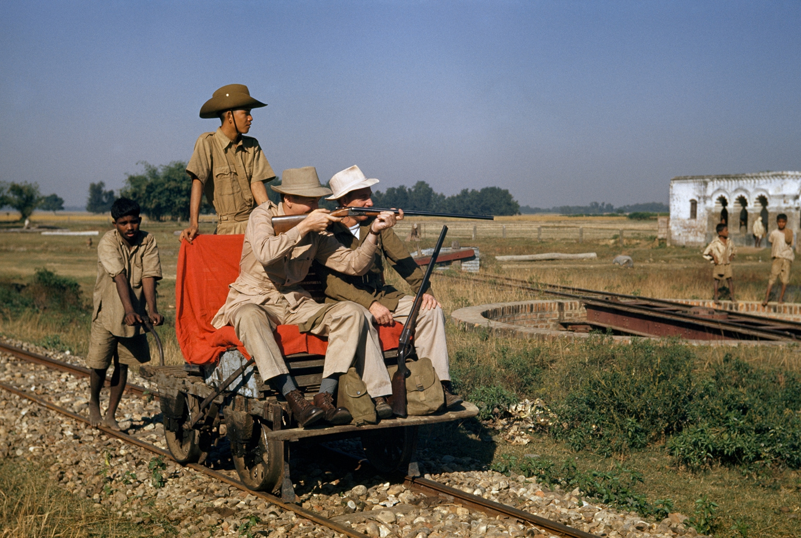 American scientists hunting birds ride in handcar pushed by laborer.