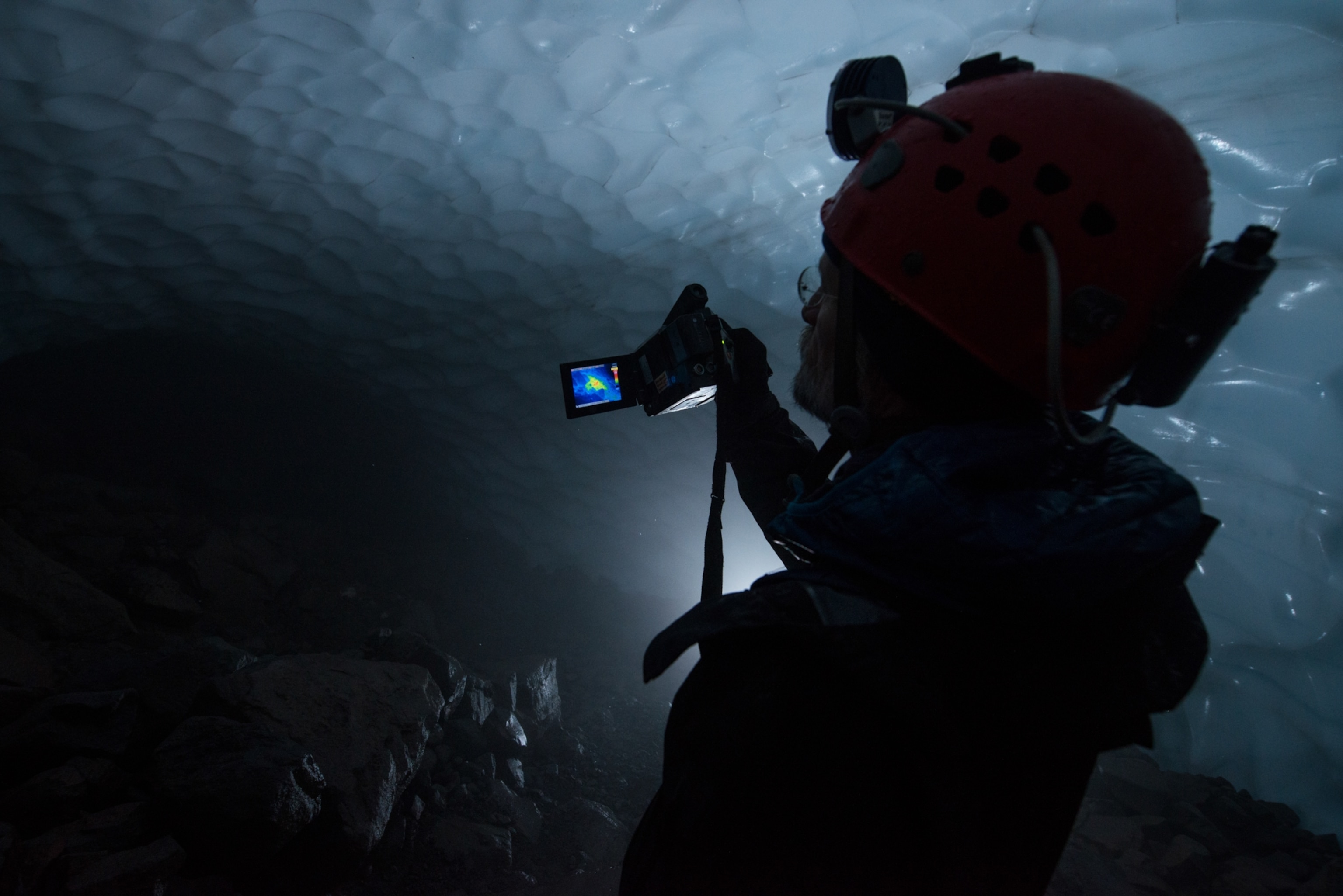 An expedition member holds up an IR camera which is capturing a heat map of an ice tunnel.
