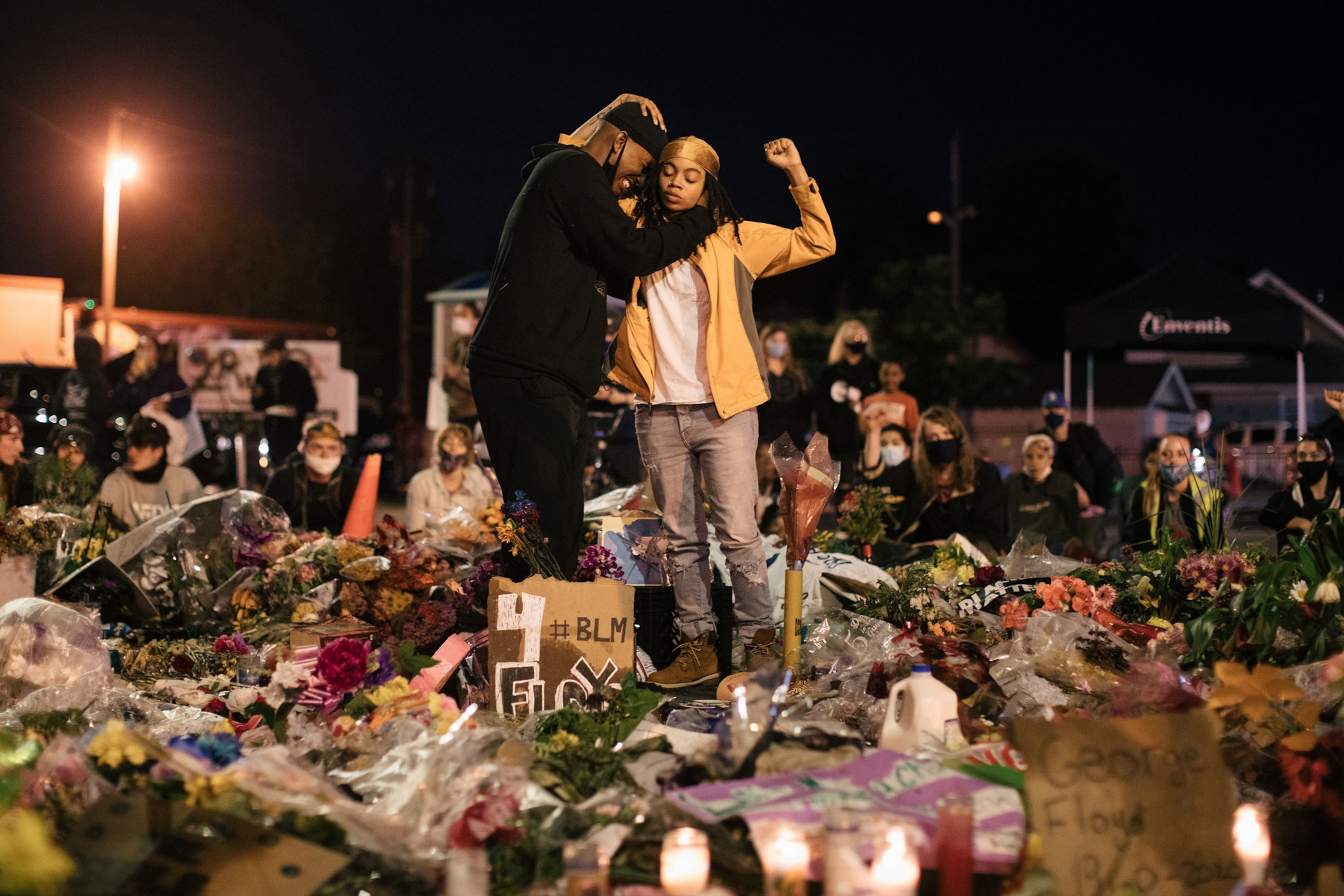 a woman raising her fist in a makeshift memorial for George Floyd